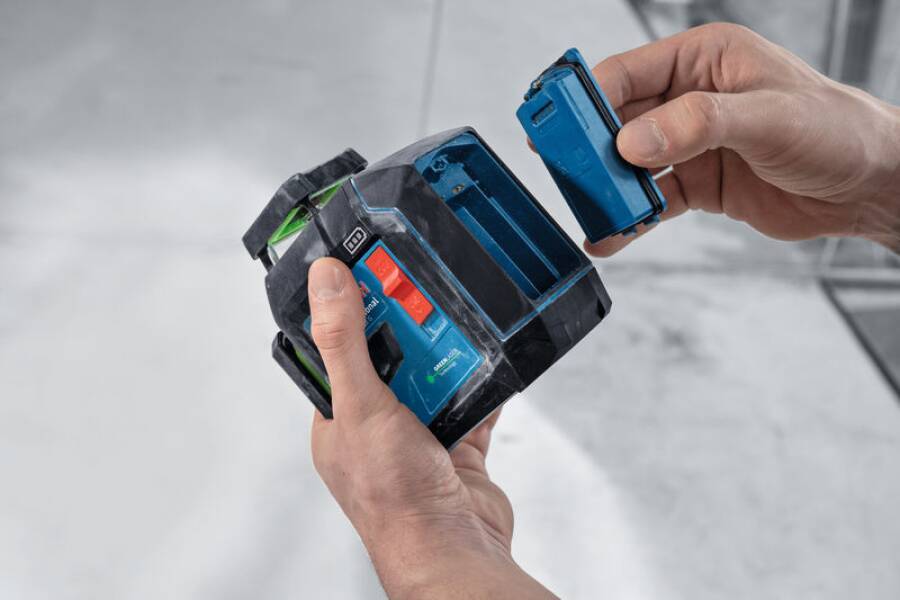 Eine Person, die demonstriert, wie eine blaue Batterie in ein schwarz-grünes elektronisches Gerät eingelegt wird, wobei der Batterieeinschub hervorgehoben wird.