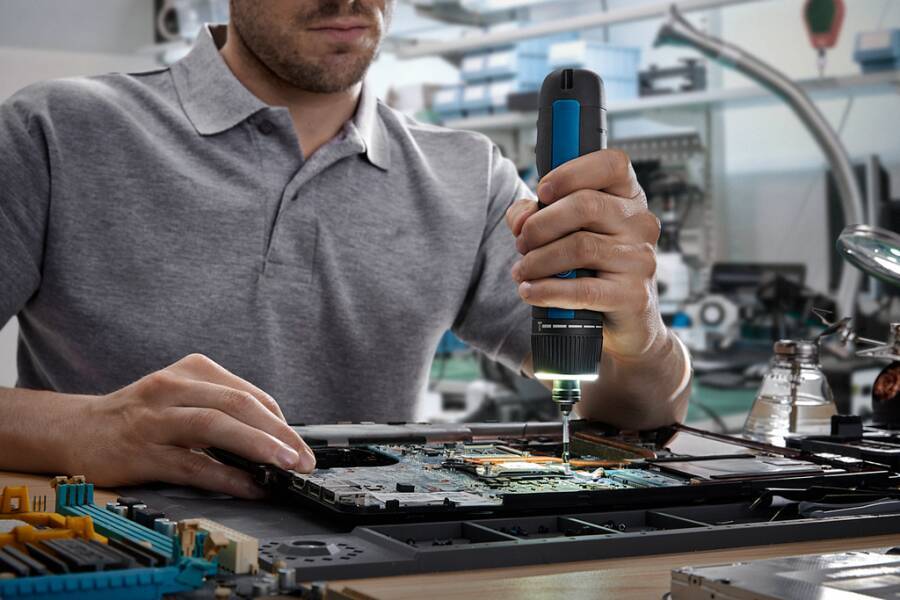 Eine Person benutzt einen Bohrer, um eine Computerplatine in einer Werkstattumgebung zu reparieren.