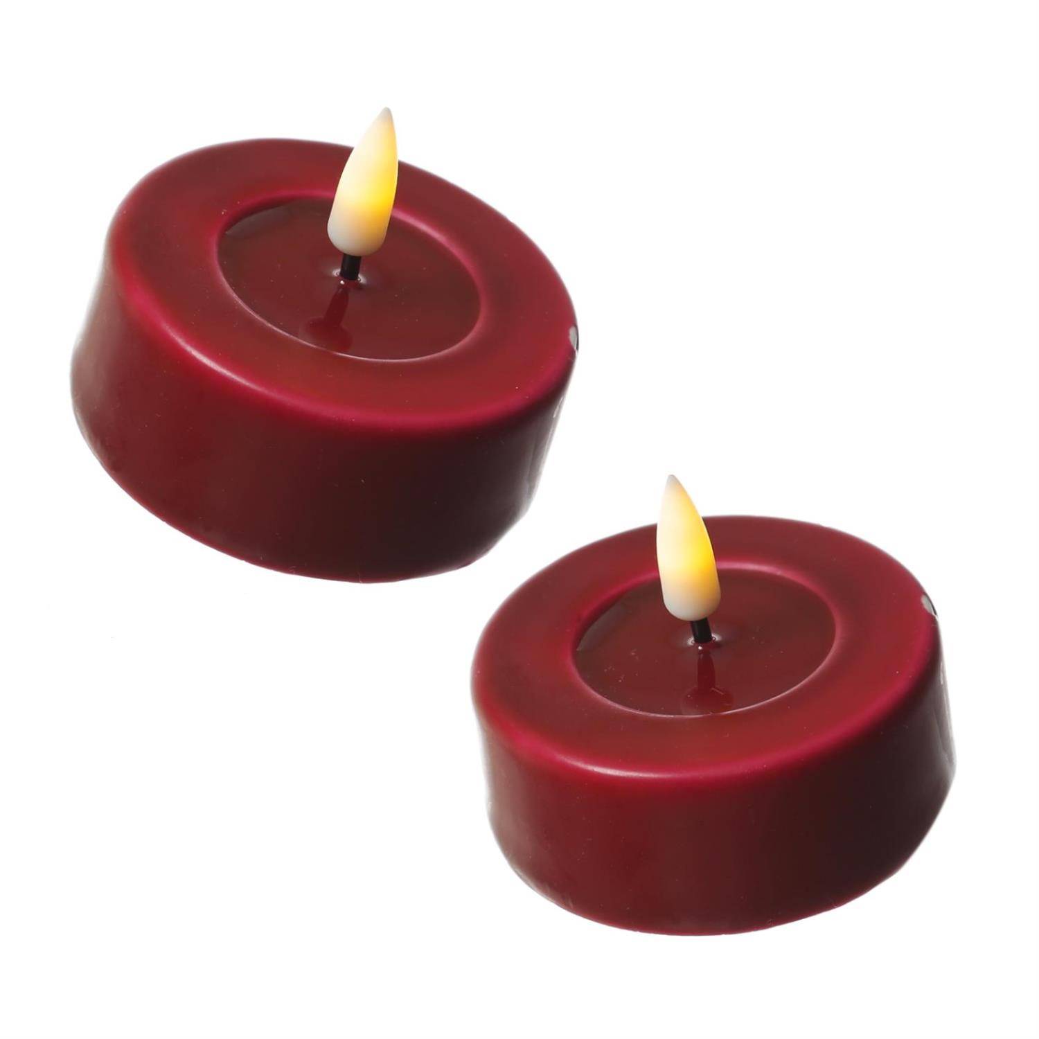 Zwei kleine, kreisrunde rote Kerzen mit gelben Flammen sind diagonal auf einem weißen Hintergrund platziert.