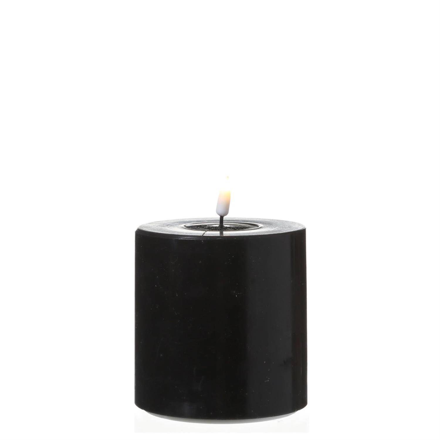 Eine schwarze Säulenkerze mit einer kleinen Flamme an der Spitze, vor einem schlichten weißen Hintergrund.