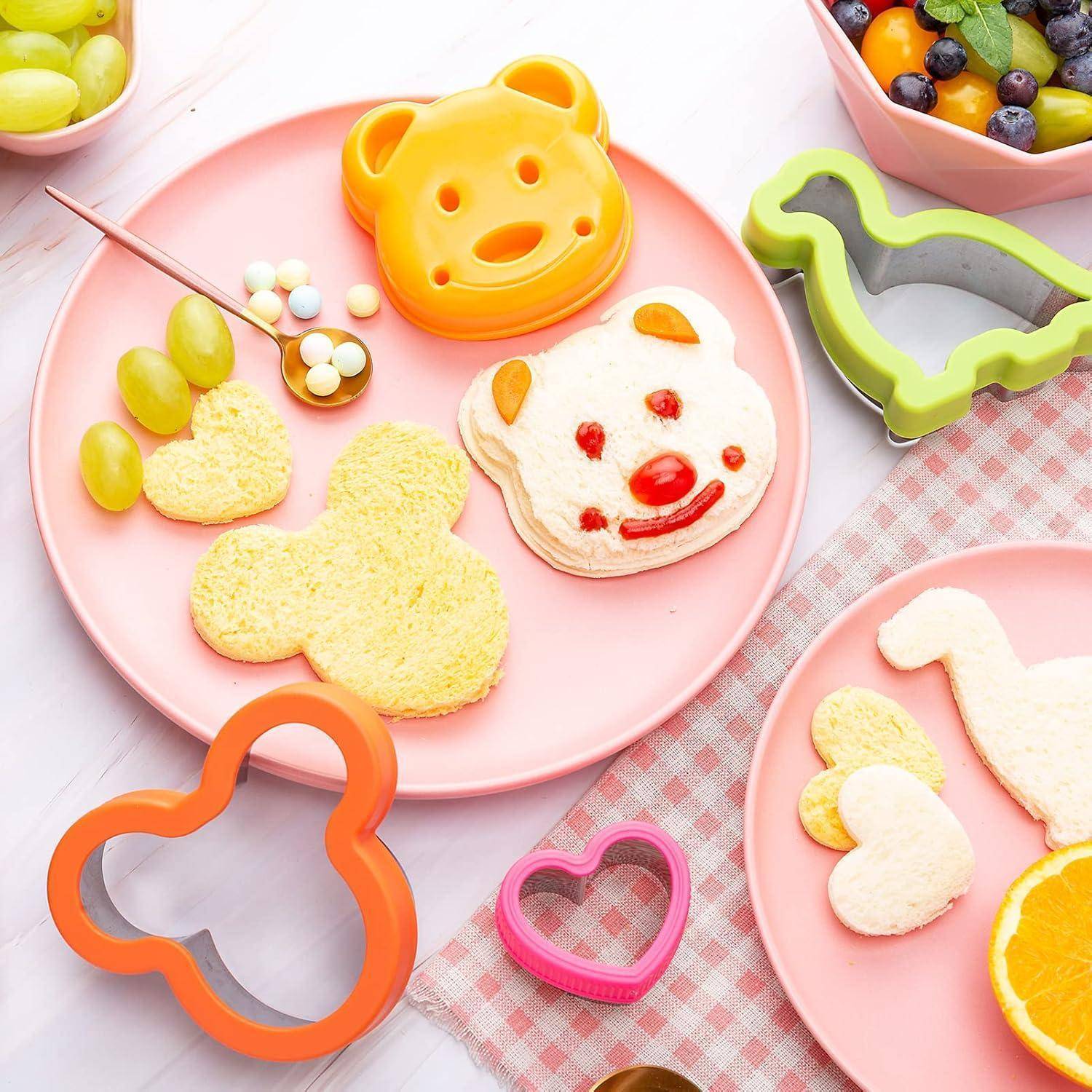 Teller mit bärenförmigen Sandwiches und Obst; farbenfrohe Ausstechformen daneben.
