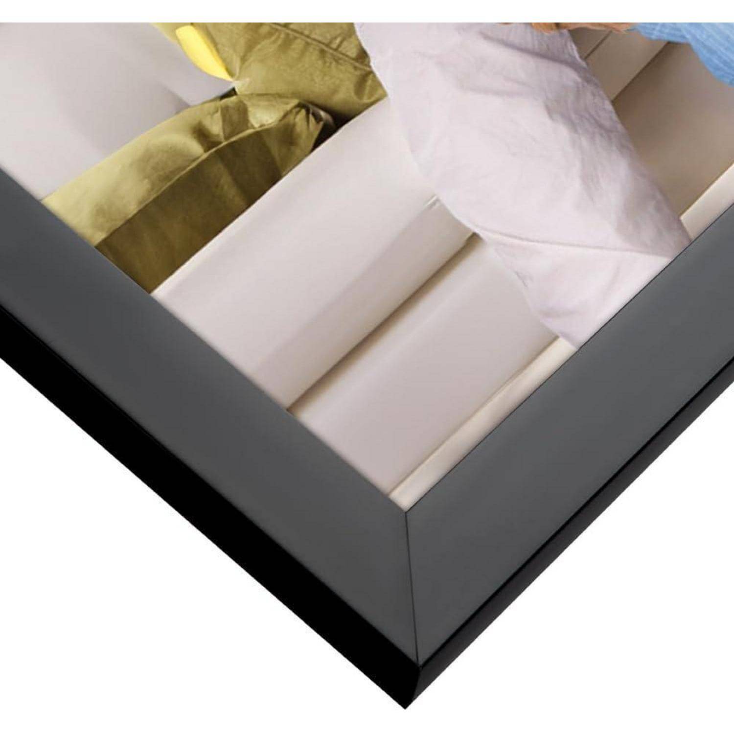 Ecke eines Rahmens, der einen Abschnitt eines pastellfarbenen Sofas mit grünen Kissen zeigt und das elegante schwarze Rahmendesign hervorhebt.