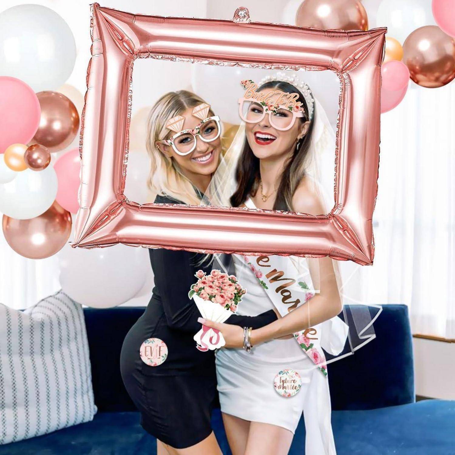 Zwei lächelnde Frauen posieren mit einem rosa Ballonrahmen, tragen 