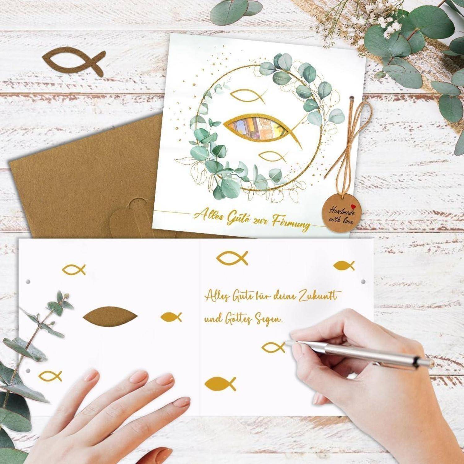 Eine Hand schreibt auf einer offenen Grußkarte mit einem Goldfisch-Symbol und deutschem Text. Ein dekorierter Umschlag und eine Karte liegen daneben.