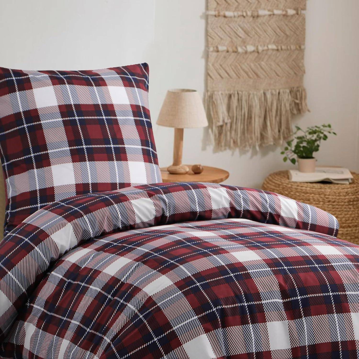 Bett mit rot-weiß karierter Bettwäsche, neben einem Nachttisch mit einer Lampe und einer kleinen Pflanze. Gewebte Wandbehängung im Hintergrund.