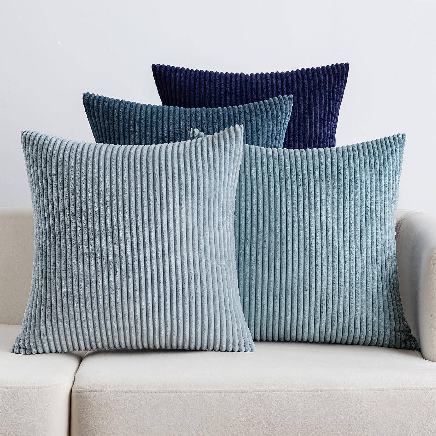 Ein beige Sofa mit vier gerippten Samtakzentकissen in Blau- und Marinefarbtönen, in zwei Reihen angeordnet für einen modernen und gemütlichen Look.