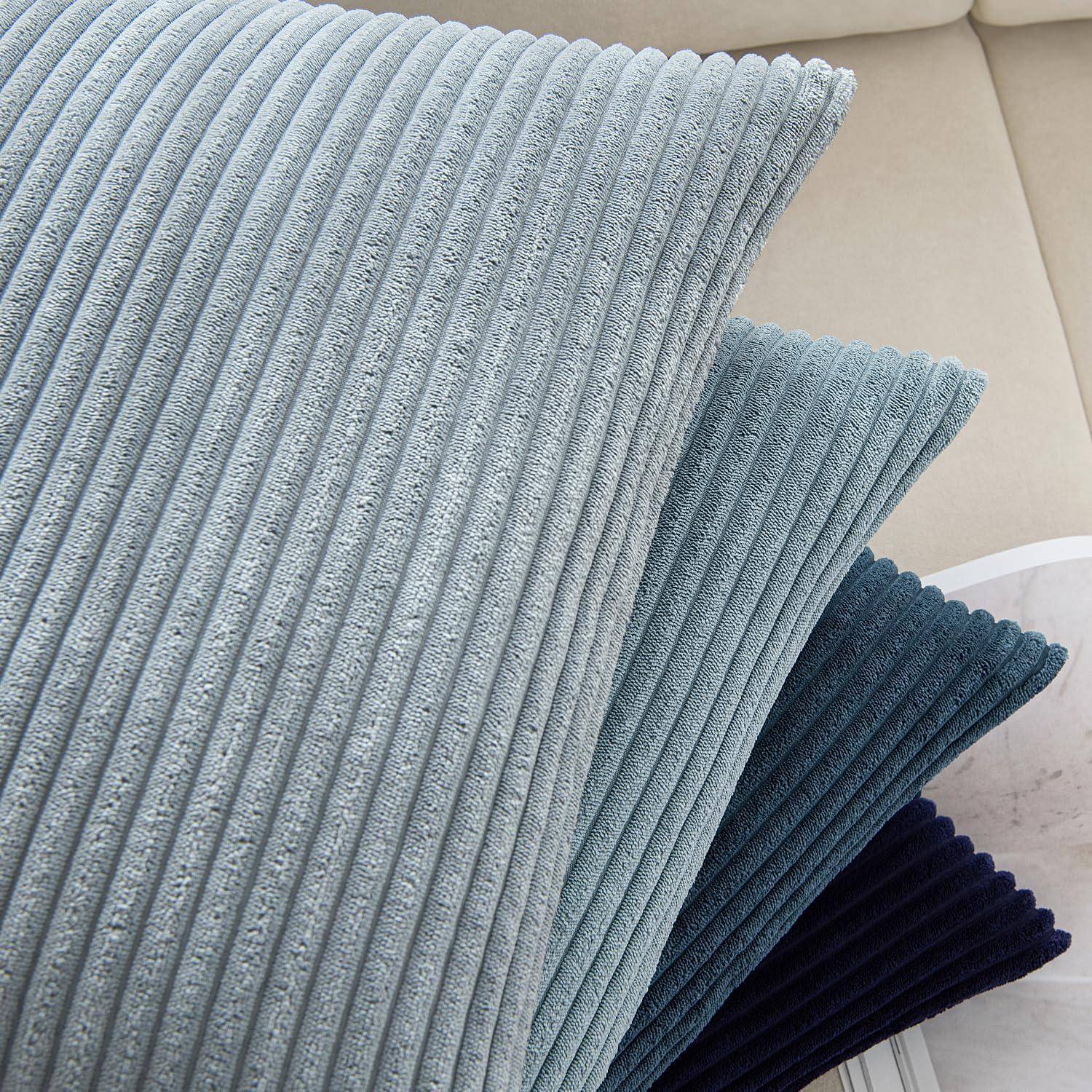 Drei gerippte Stoffkissen, die auf einem beigen Sofa gestapelt sind, in Schattierungen von Hellblau, Petrol und Marineblau, die Textur und Farbkontrast hinzufügen.