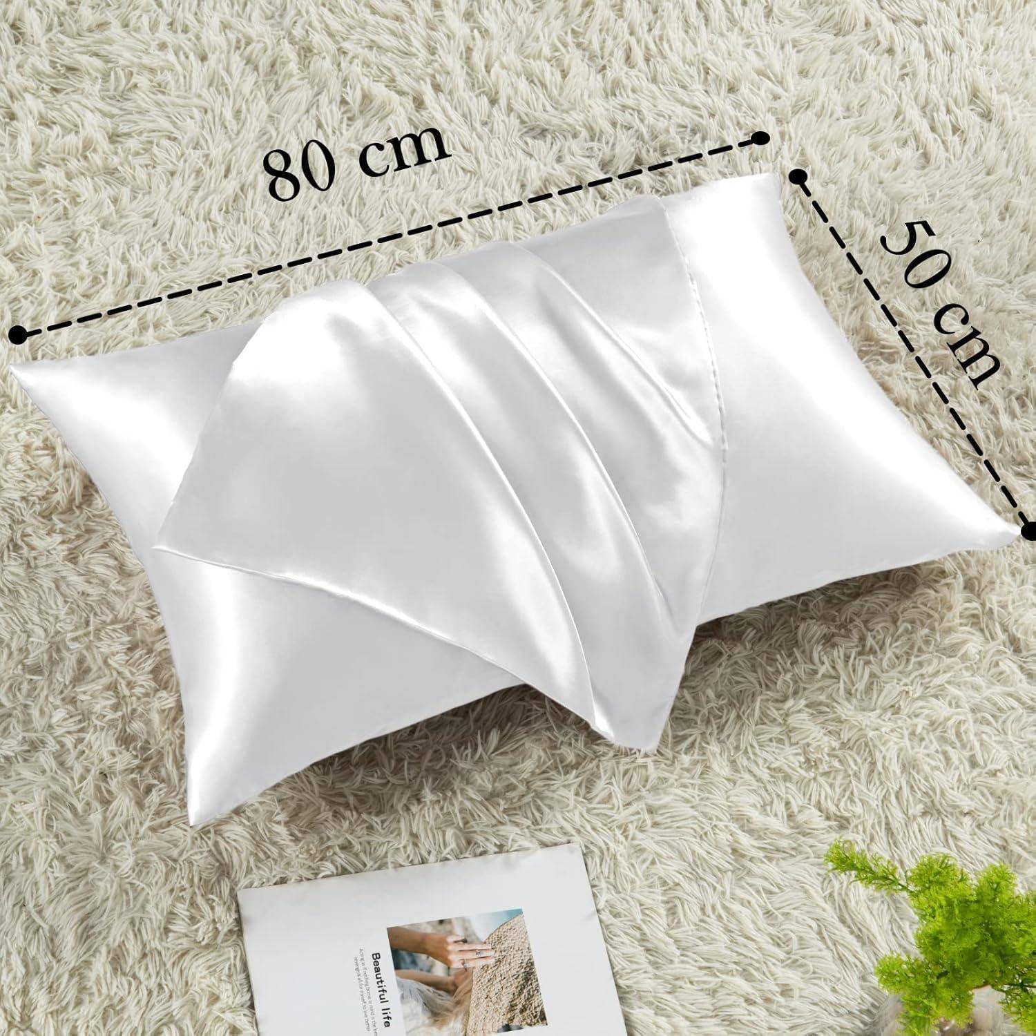 Weißes Satin-Kopfkissen mit den Maßen 80 cm x 50 cm auf einer strukturierten beigen Oberfläche, neben einer aufgeschlagenen Zeitschrift.