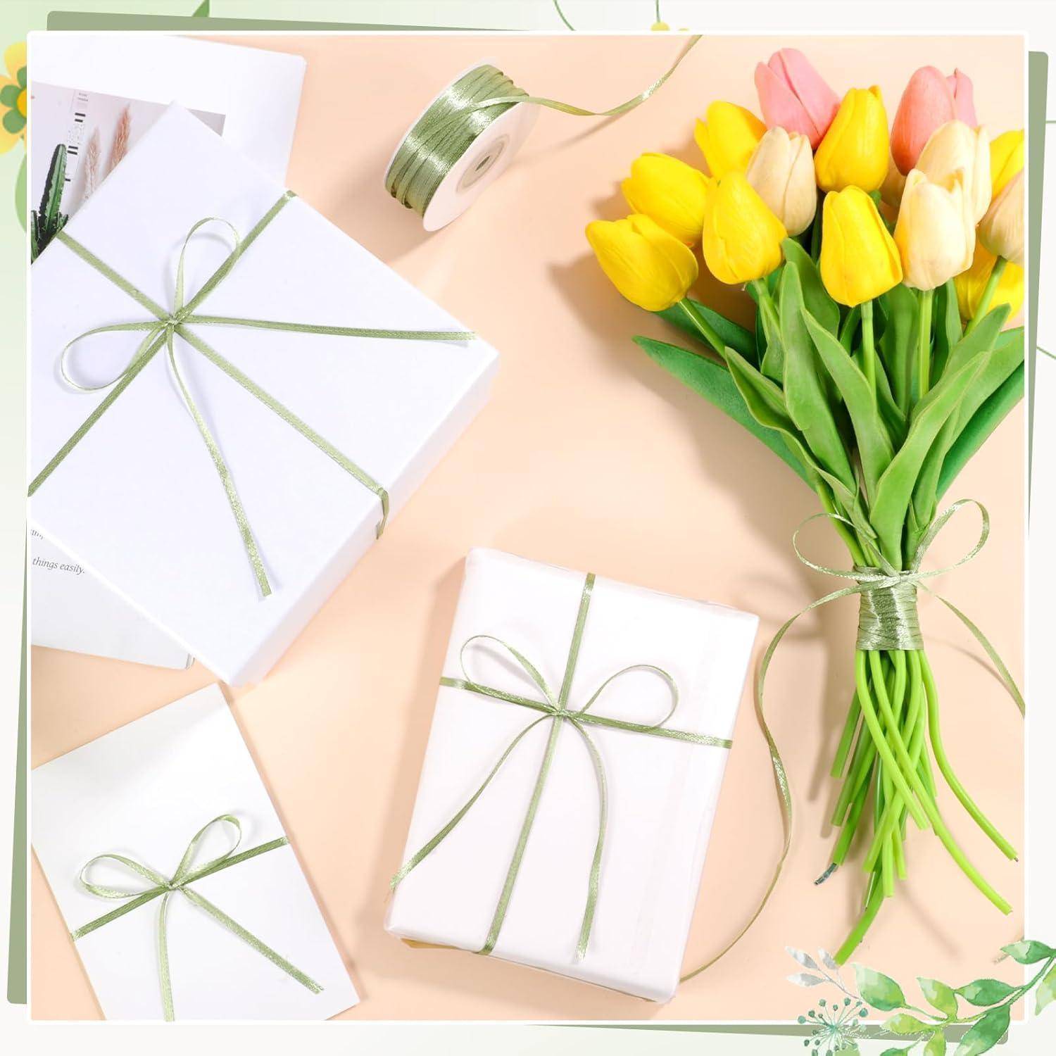 Ein Blumenstrauß aus gelben und rosa Tulpen liegt neben drei weißen Geschenkkartons, die mit grünem Band verschlossen sind, vor einem hellen Pfirsichhintergrund.