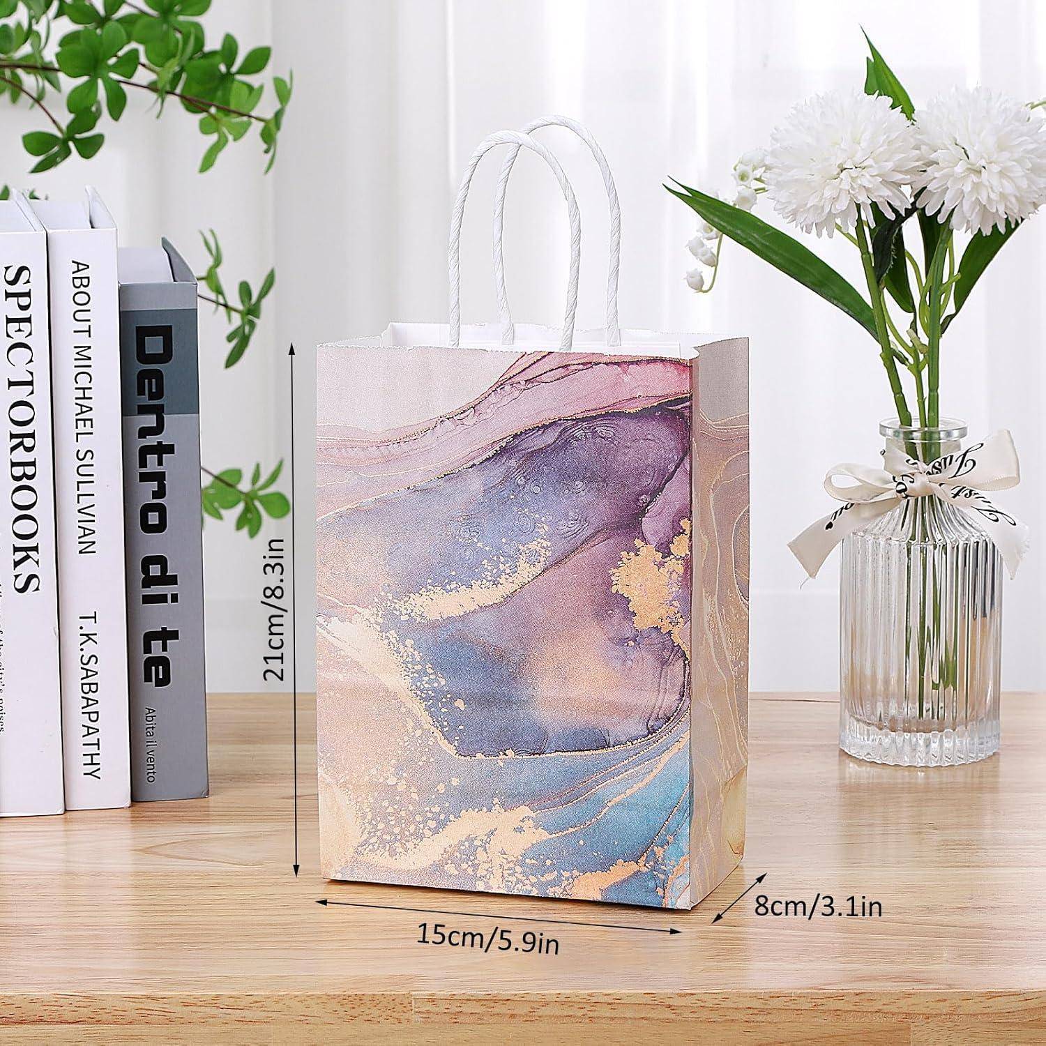 Eine bunte Papiertasche mit abstraktem Design und beschrifteten Abmessungen: Höhe 23 cm/9,1 Zoll, Breite 15 cm/5,9 Zoll, Tiefe 8 cm/3,1 Zoll auf einem Tisch.
