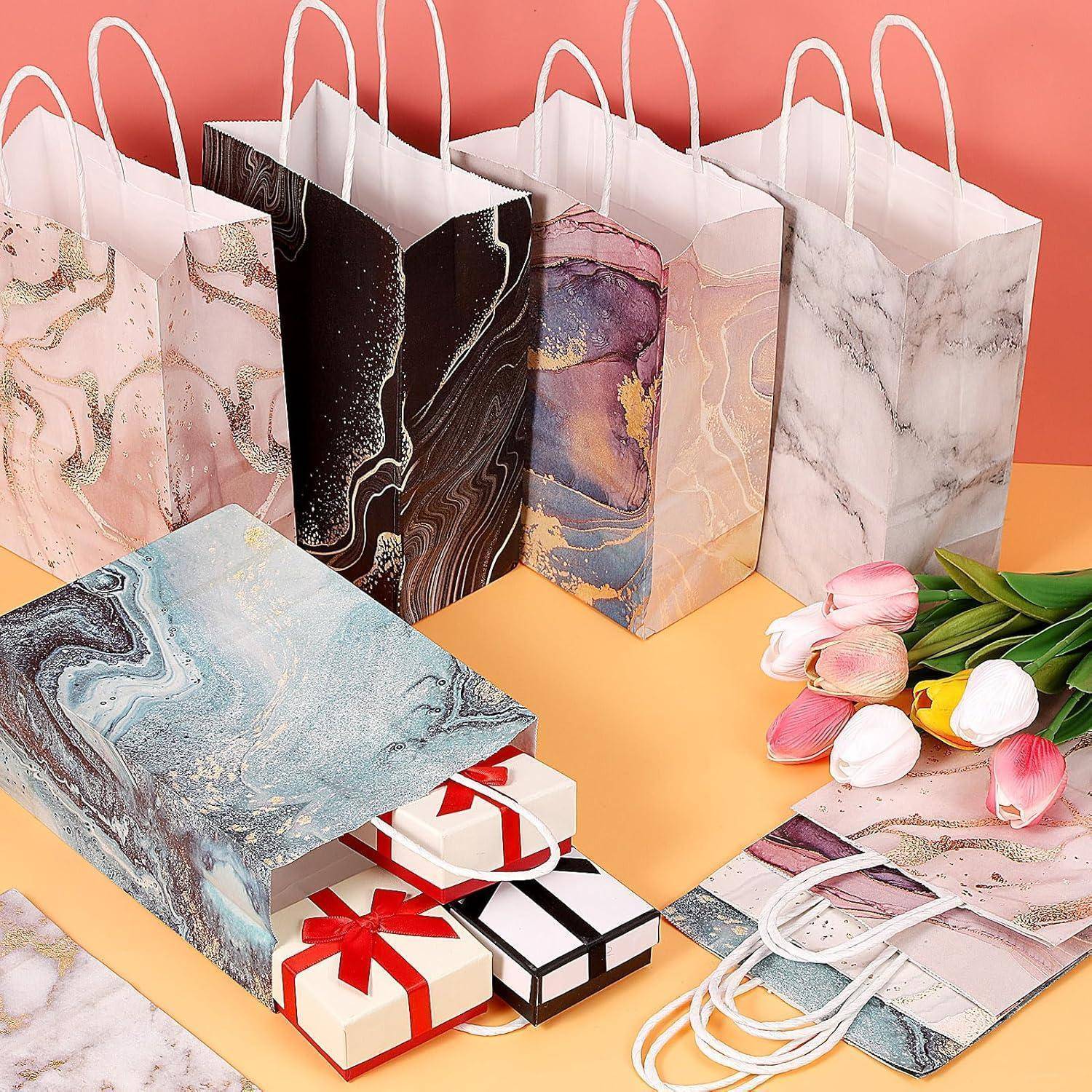 Geschenktüten mit abstrakten Designs in verschiedenen Farben stehen aufrecht; daneben liegt eine umgekippte Tüte, aus der eingewickelte Geschenke herausfallen. Tulpen vervollständigen die Dekoration.