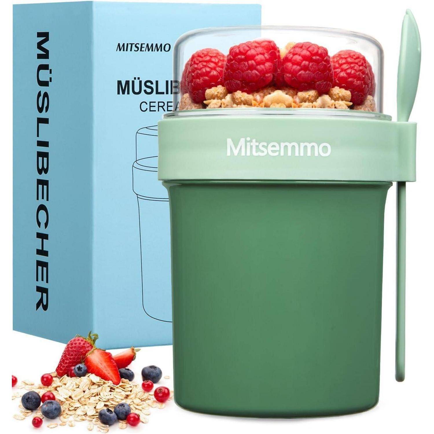 Grüner Behälter mit Müsli und Himbeeren, Löffel angehängt. 'MÜSLIBECHER'-Text auf blauer Schachtel im Hintergrund.