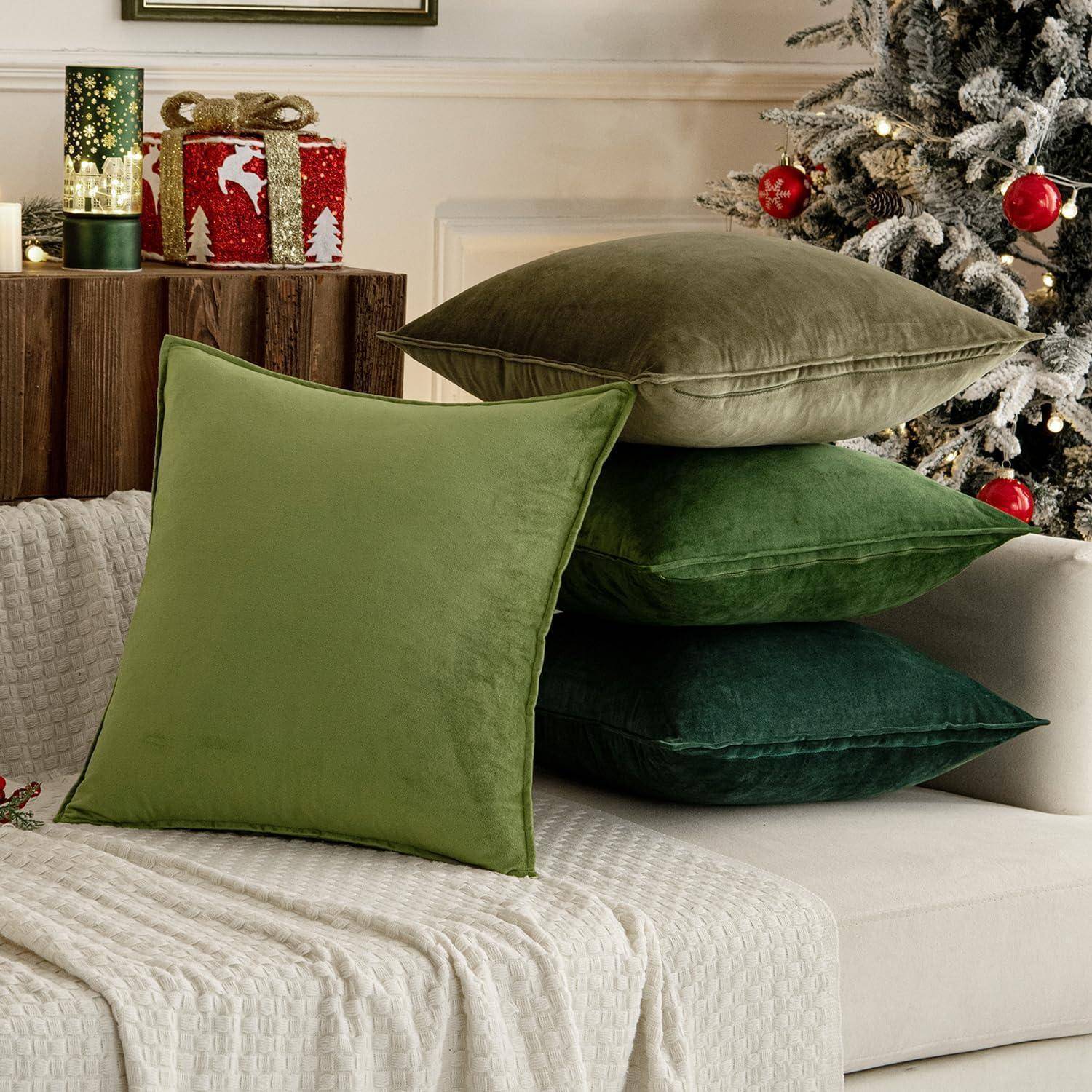 Eine gemütliche Ecke im Wohnzimmer mit einem Weihnachtsbaum, Kerzen und dekorativen roten Geschenkkartons. Grüne, samtige Kissen sind auf einem Sofa gestapelt.