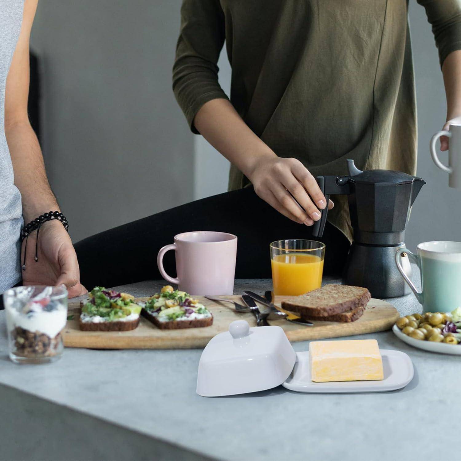 Zwei Personen bereiten Frühstück vor mit Avocado-Toast, Joghurt, Saft und Kaffee auf einer Küchenarbeitsplatte.