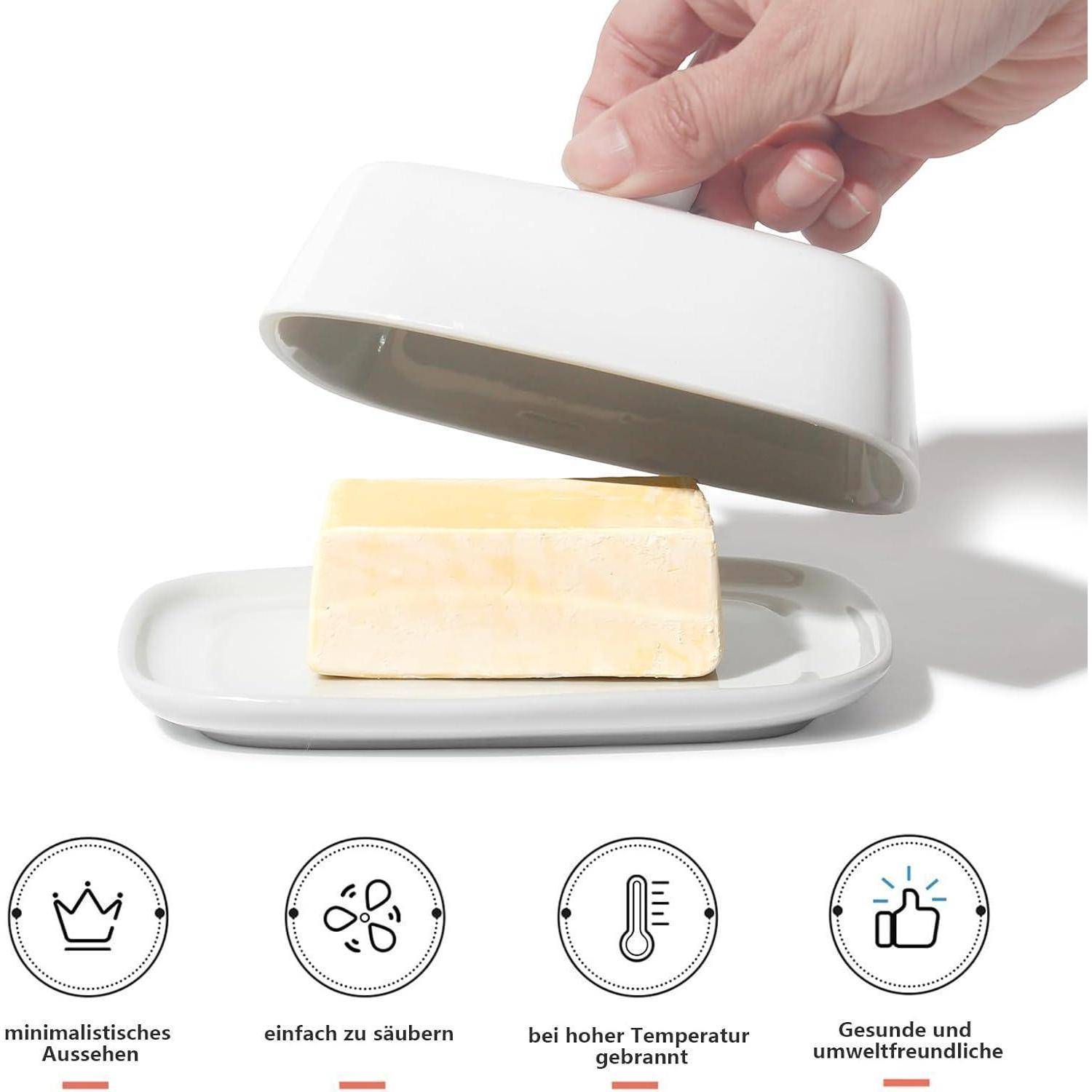 Eine Hand, die den Deckel einer weißen Butterdose mit Butter im Inneren anhebt.Icons darunter zeigen ein minimalistisches Design, leichte Reinigung, hitzebeständige Eigenschaften und Umweltfreundlichkeit.