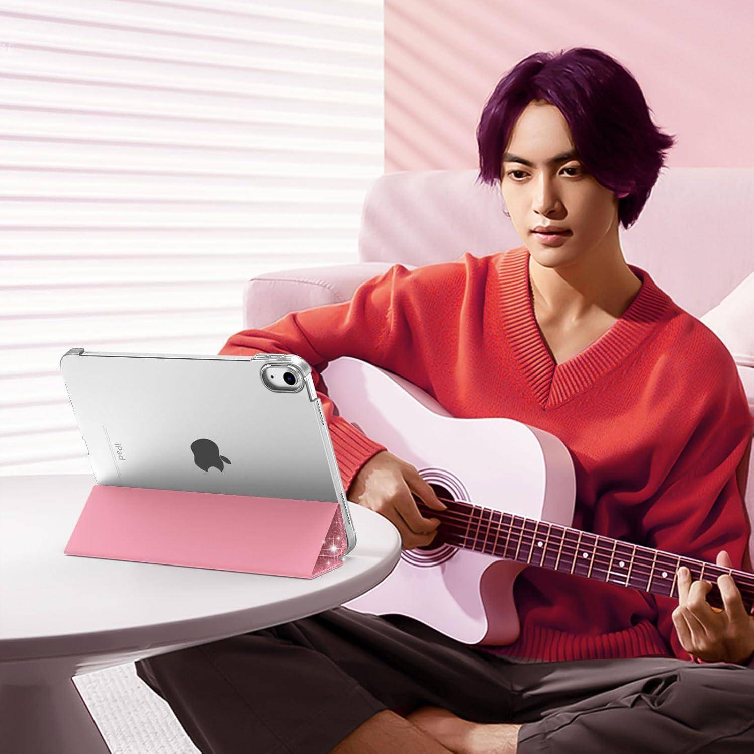 Eine Person mit violetter Haarfarbe in einem roten Pullover, die eine Akustikgitarre spielt und drinnen auf einem Stuhl sitzt, wobei ein Tablet auf einem Tisch steht.