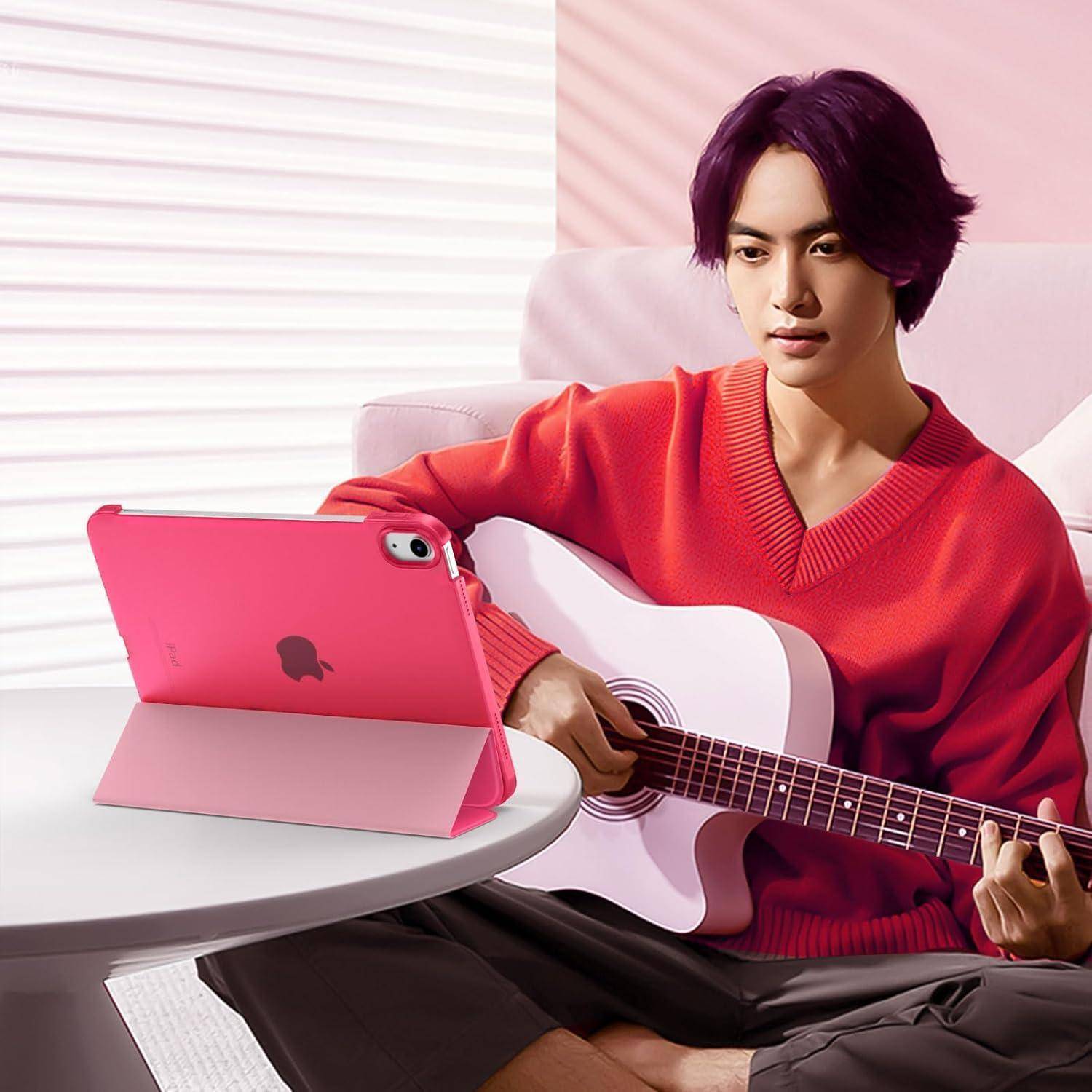 Eine Person in einem roten Pullover spielt eine Akustikgitarre in einem gemütlichen Raum, sitzt auf einem Sofa, mit einem Tablet in der Nähe aufgestellt.