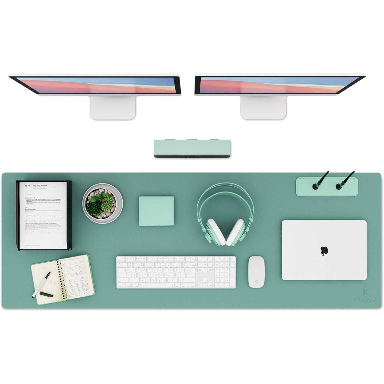 Ein ordentlich organisierter Arbeitsplatz mit zwei Monitoren, einem Laptop, drahtloser Tastatur und Maus, Kopfhörern, einem Notizbuch und einer kleinen Pflanze.