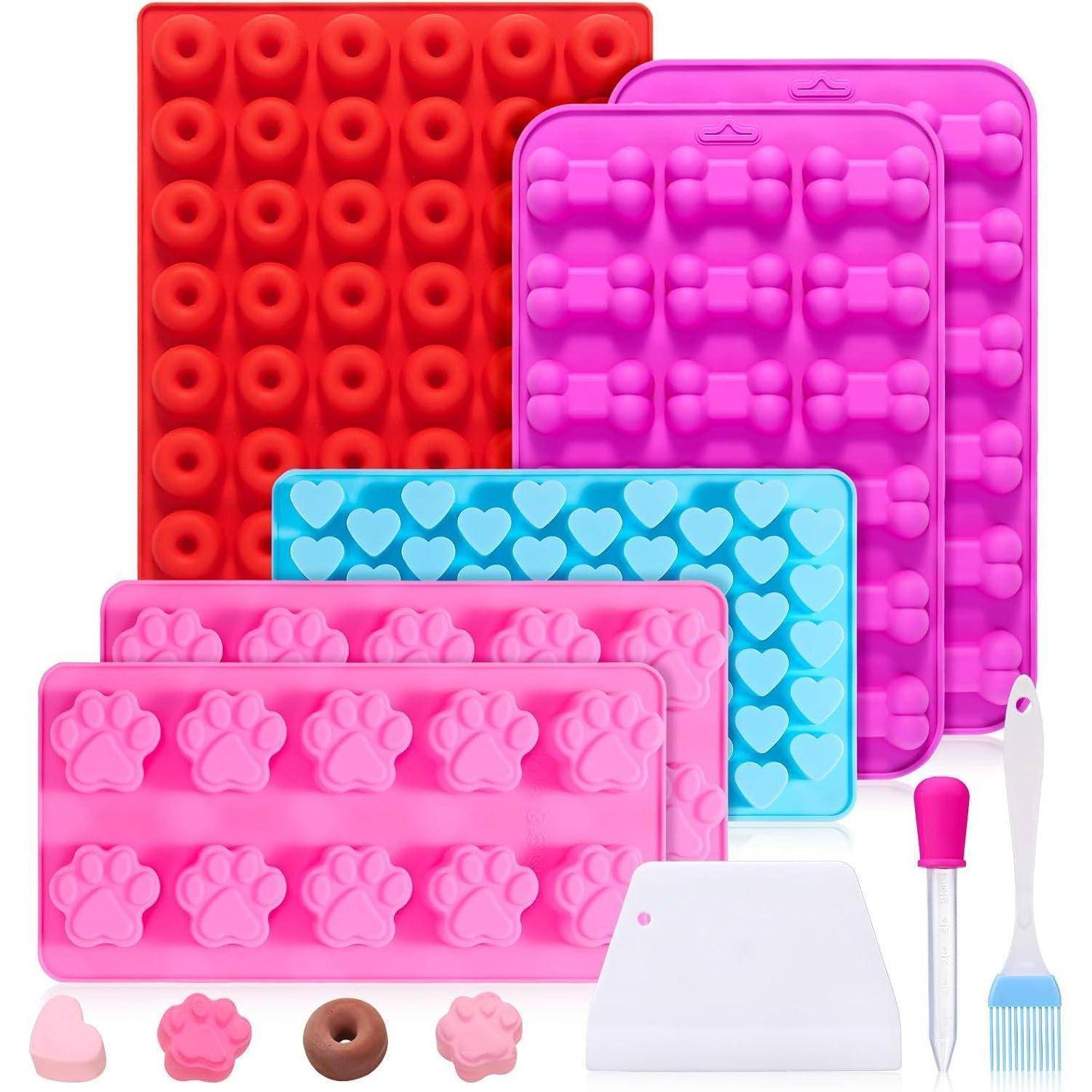 Set mit bunten Silikonbackformen, das verschiedene Formen wie Pfotenabdrücke, Herzen und Donuts umfasst. Enthält einen Spatel, eine Pipette und einen Schaber.
