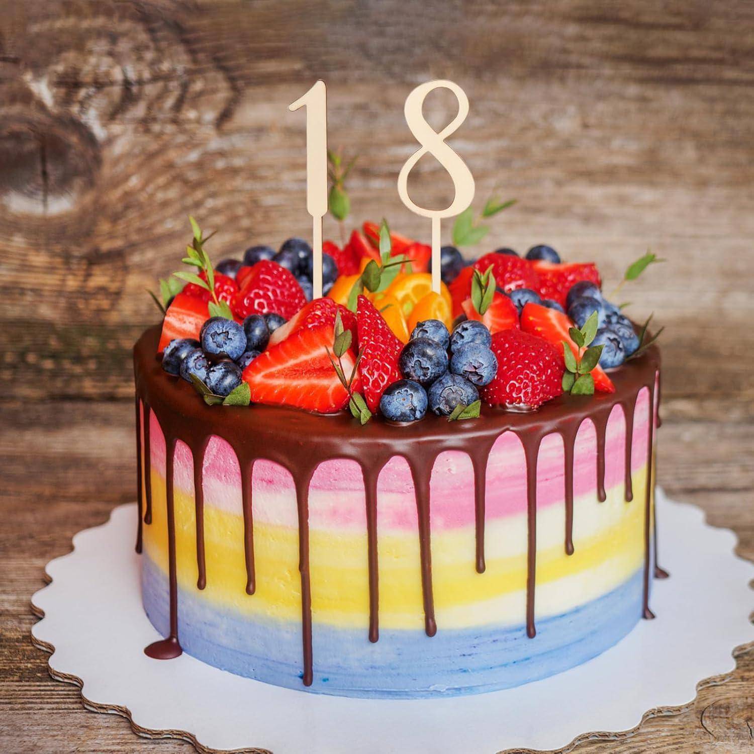 Bunter Kuchen mit Schokoladenüberzug, verziert mit Erdbeeren, Blaubeeren und Kerzen in Form der Zahl '18', auf einem rustikalen Holzuntergrund.