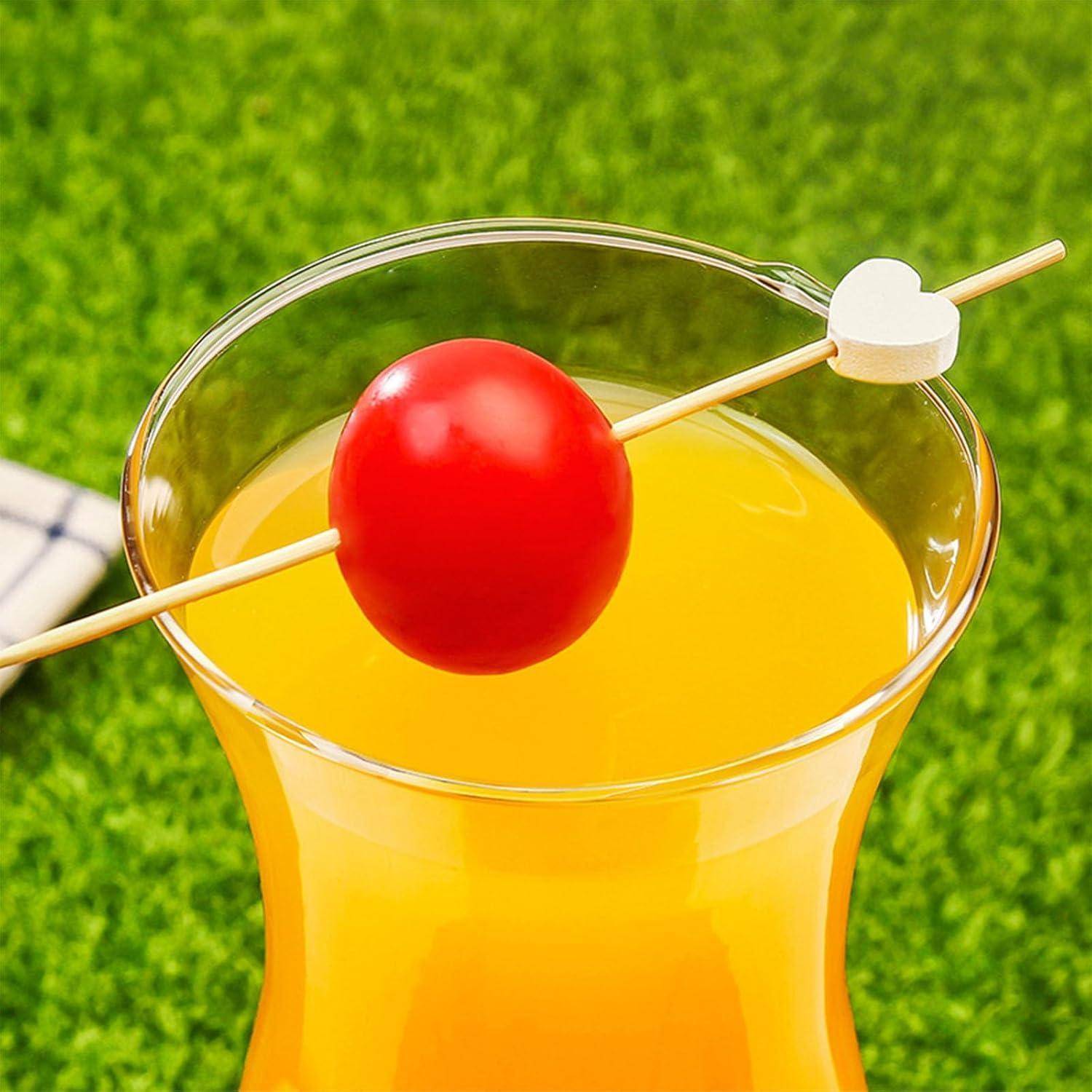 Ein Glas Orangensaft auf Gras, garniert mit einer Kirsche an einem Spieß, gekrönt von einer weißen Herzform.