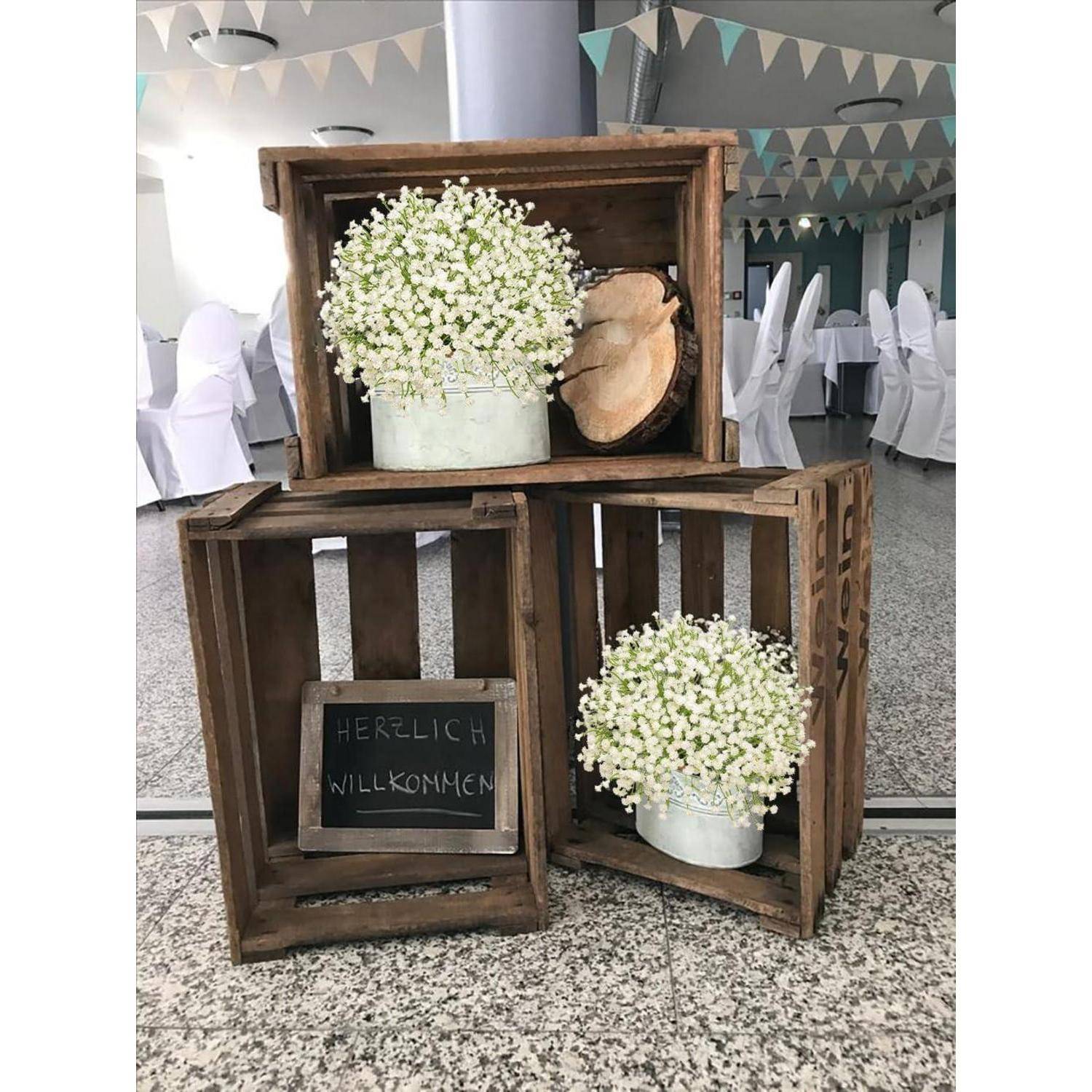 Holzkisten aufgereiht mit zwei Vasen mit weißen Blumen und einer kleinen Tafel mit dem Text 