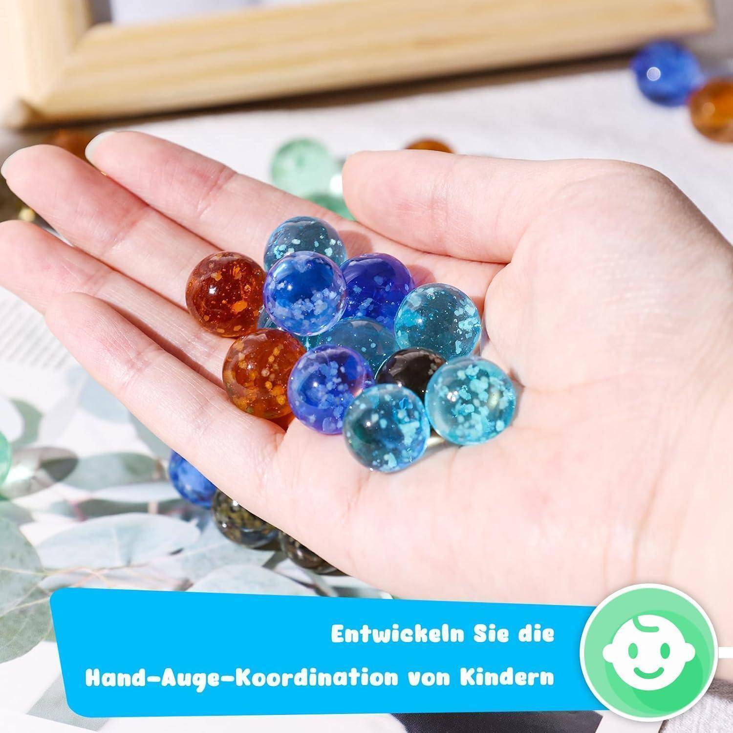 Eine Hand, die bunte Glasmurmeln hält. Ein Banner darunter liest sich: 'Entwickeln Sie die Hand-Auge-Koordination von Kindern' mit einem lächelnden Symbol.