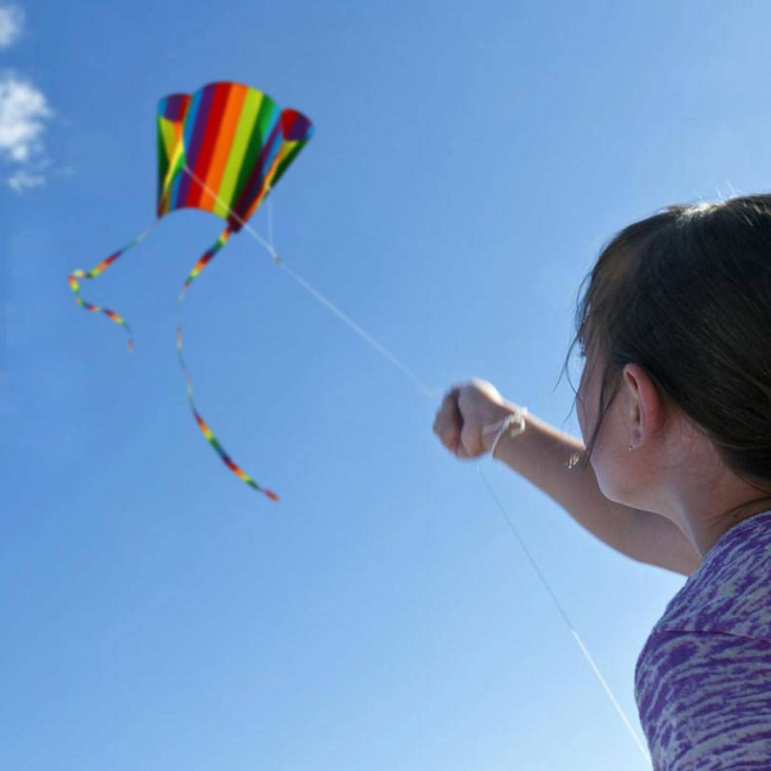 Eine Person, die einen bunt gestreiften Drachen vor einem klaren blauen Himmel fliegt.
