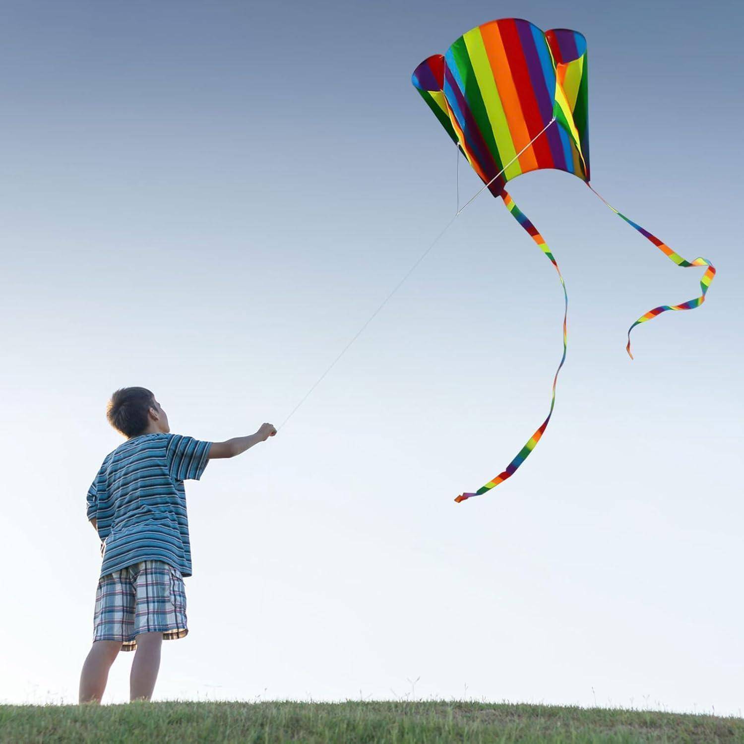Ein Kind fliegt einen bunten, gestreiften Drachen am klaren blauen Himmel und steht dabei auf einem grasbedeckten Hügel, was Freiheit und Freude symbolisiert.