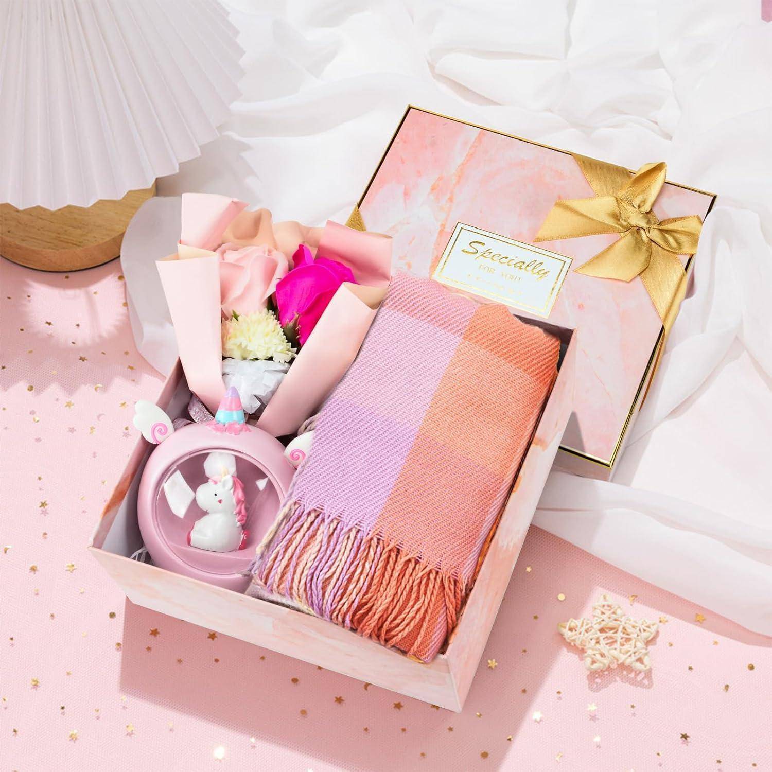 Geschenkbox mit einem rosa und orangefarbenen karierten Schal, einem Blumenstrauß und einem dekorativen rosa Teller mit Tiermotiv. Die Box ist mit einem goldenen Band geschmückt.