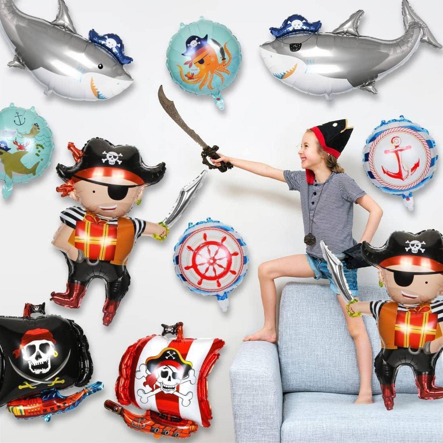 Mädchen mit Piratenhut sitzt auf einem Sofa und hält ein Spielzeug-Schwert, umgeben von Piraten- und nautischen Luftballons.