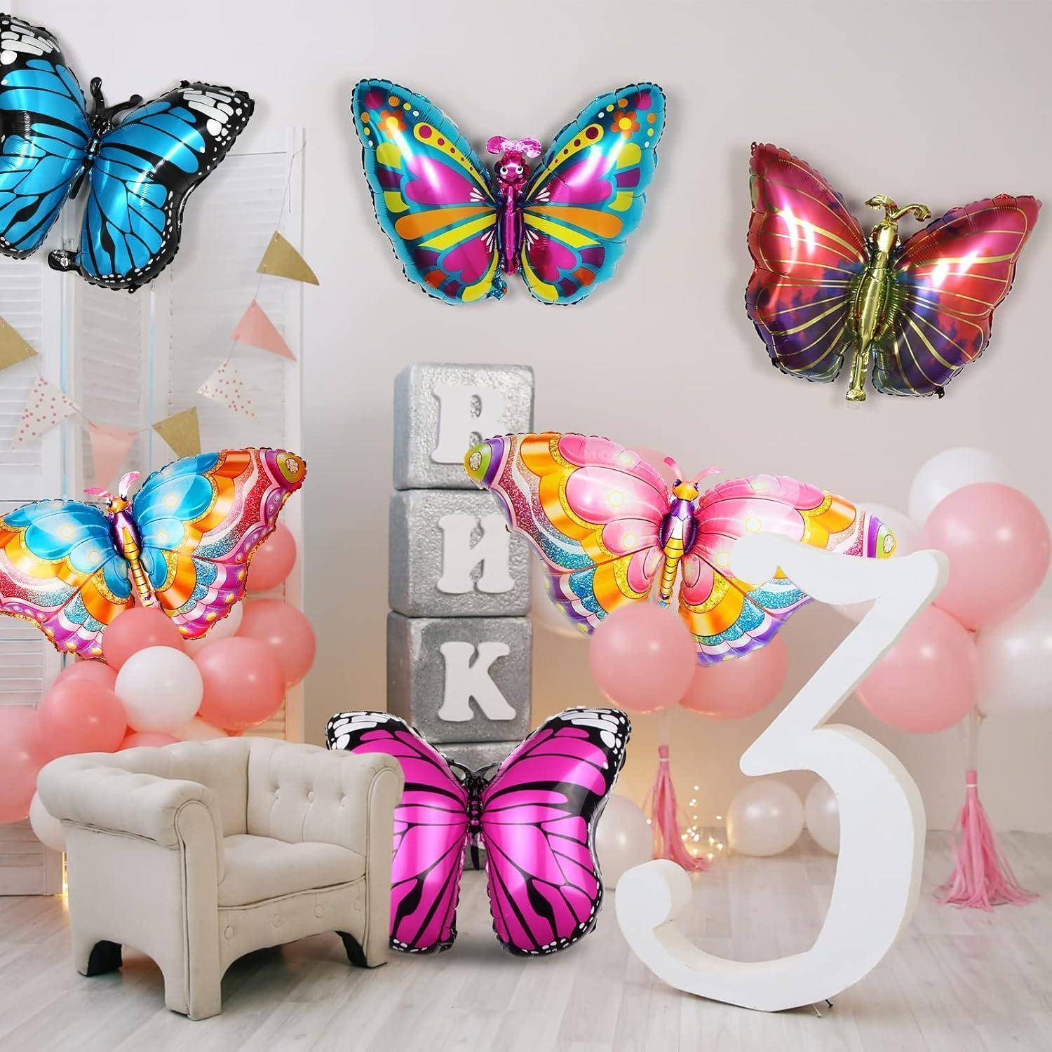Bunte Schmetterlingsdekorationen an einer Partywand mit Luftballons und einer großen Zahl '3', neben einem weißen Stuhl und pastellrosa Luftballons.