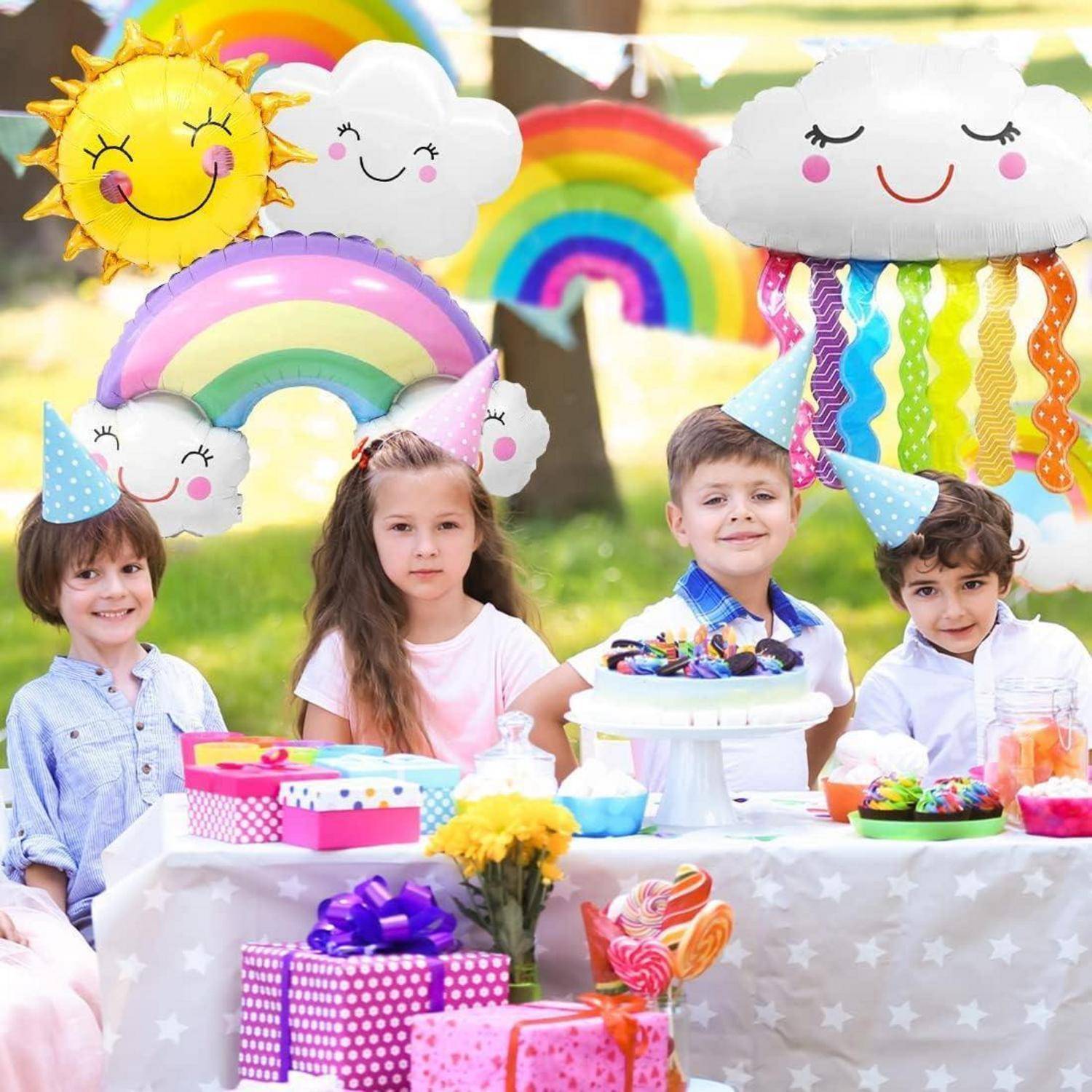 Kinder mit Partyhüten sitzen an einem festlichen Tisch mit einer Geburtstagstorte. Bunte Dekorationen umfassen Regenbogen- und Sonnenballons im Hintergrund.