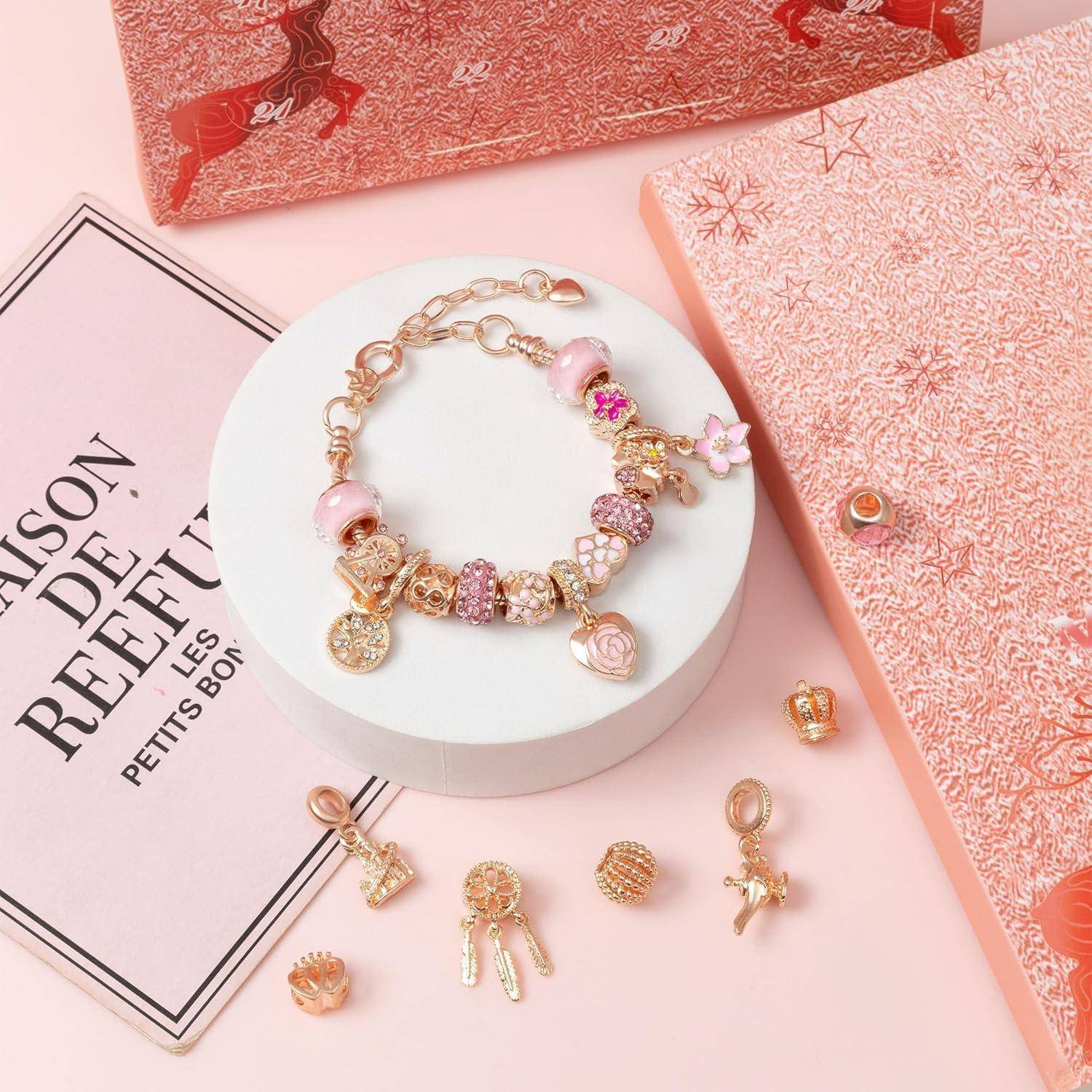 Ein Bettelarmband mit rosa und goldenen Zierperlen wird neben einem rosafarbenen Notizbuch mit Sternmuster und zusätzlichen Anhängern präsentiert.
