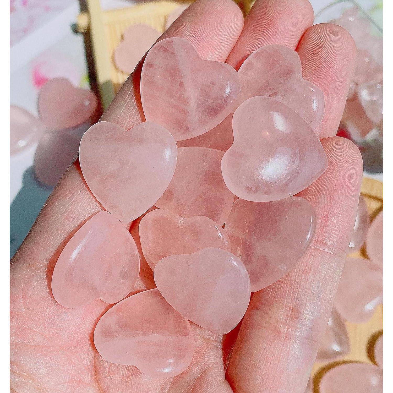 Eine Hand hält transluzente, herzförmige Steine in Rosa, höchstwahrscheinlich Rosenquarz, mit einer weichen, sanften Erscheinung. Im Hintergrund sind zusätzliche Steine verstreut.