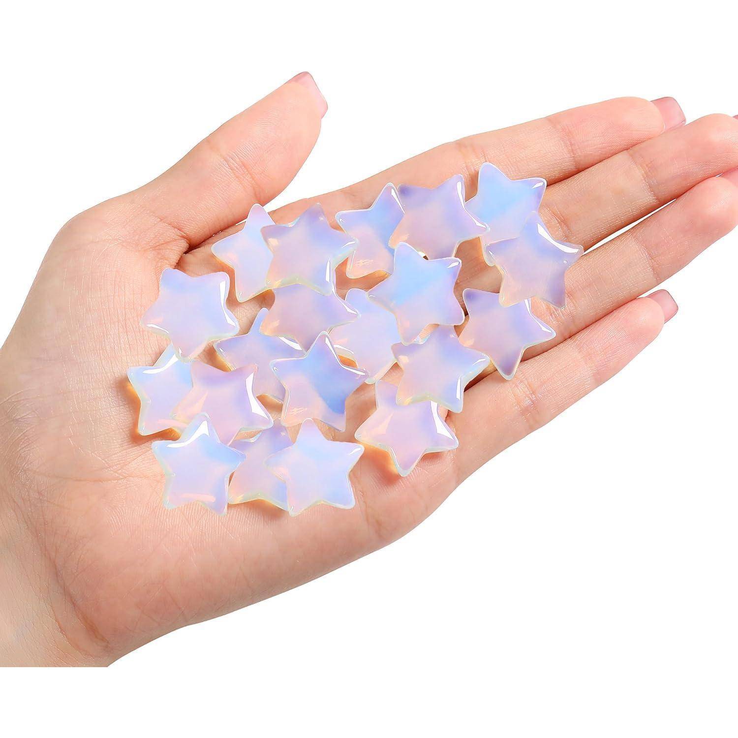 Eine Hand hält mehrere kleine, durchscheinende sternförmige Objekte, die opalesierend wirken und pastellfarbene Reflexe zeigen.