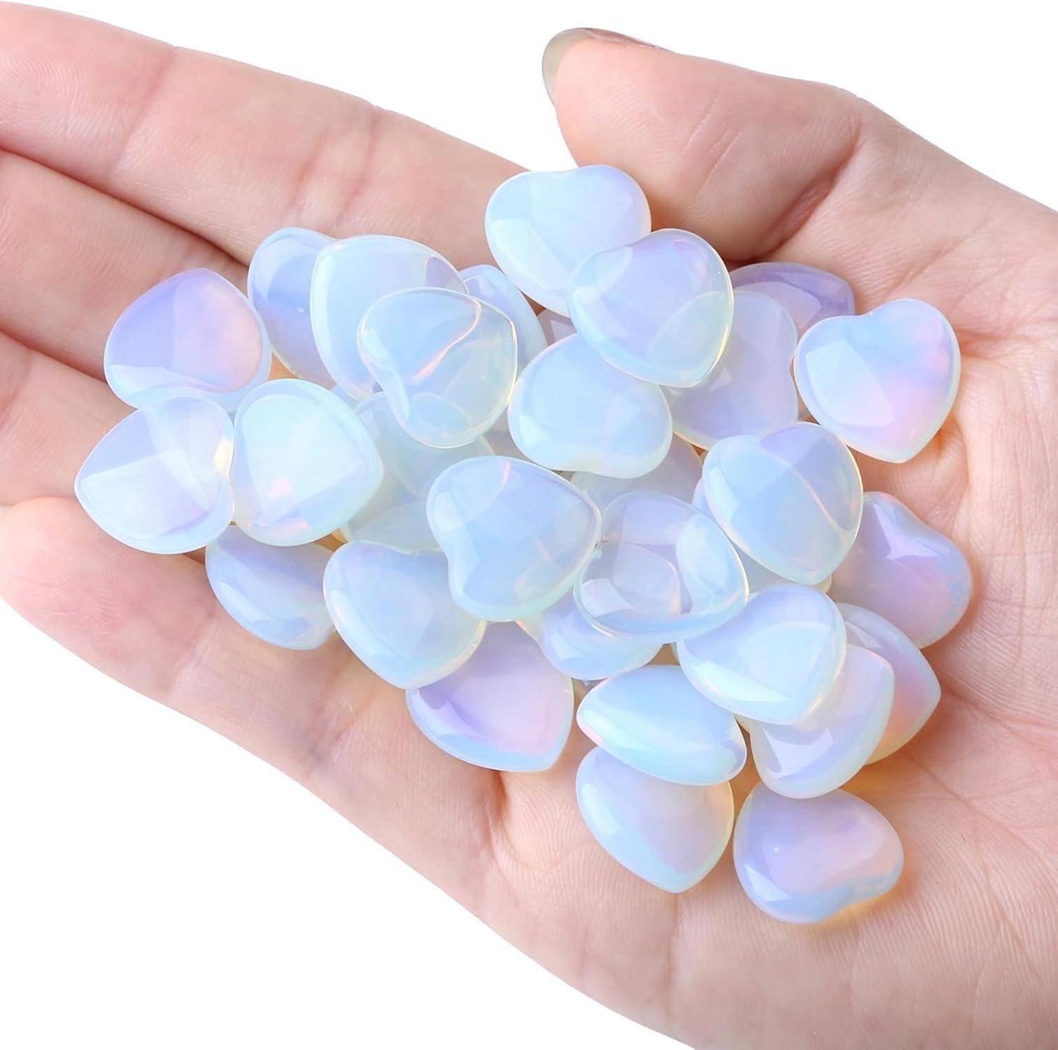 Eine Hand hält mehrere kleine schillernde, herzförmige Steine, die das Licht in Blau- und Rosatönen reflektieren und Liebe und Ruhe symbolisieren.