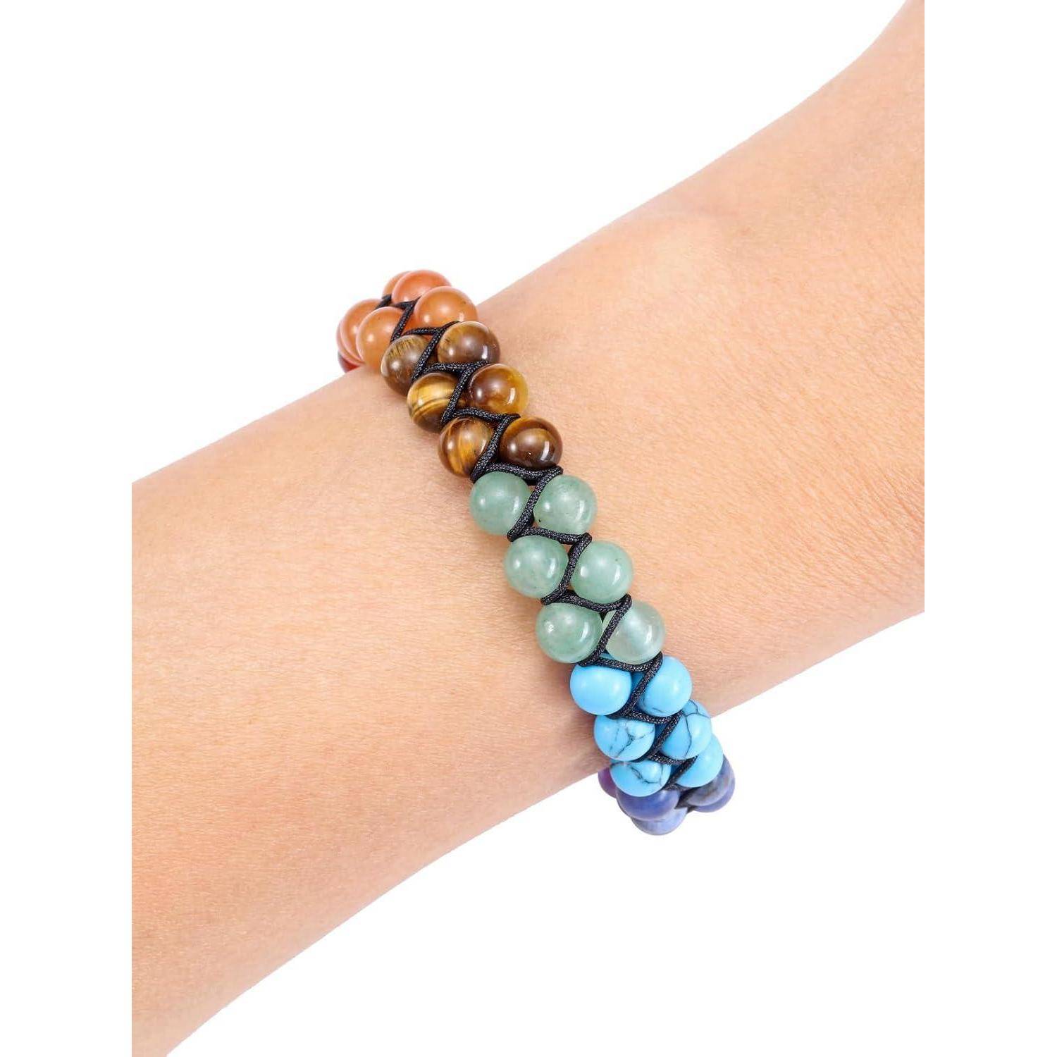 Ein Handgelenk, das ein Perlenarmband mit Steinen in Braun-, Grün- und Blautönen trägt, die von warmen zu kühlen Tönen in einem Farbverlauf angeordnet sind.