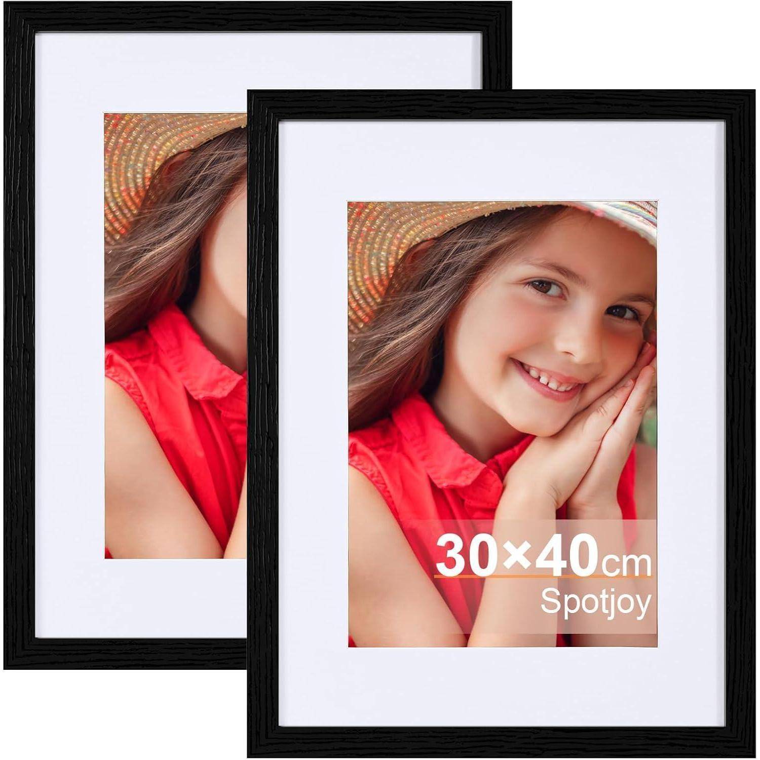 Zwei schwarzgerahmte Fotorahmen, die jeweils ein Porträt eines lächelnden jungen Mädchens mit Hut zeigen, mit dem Text '30x40 cm Spotjoy'.