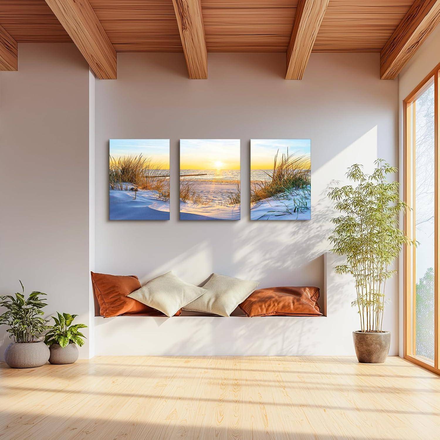 Ein gut beleuchteter Wohnraum zeigt drei strandbezogene Gemälde an der Wand über einer Holzbank mit weißen und braunen Kissen, neben Topfpflanzen.