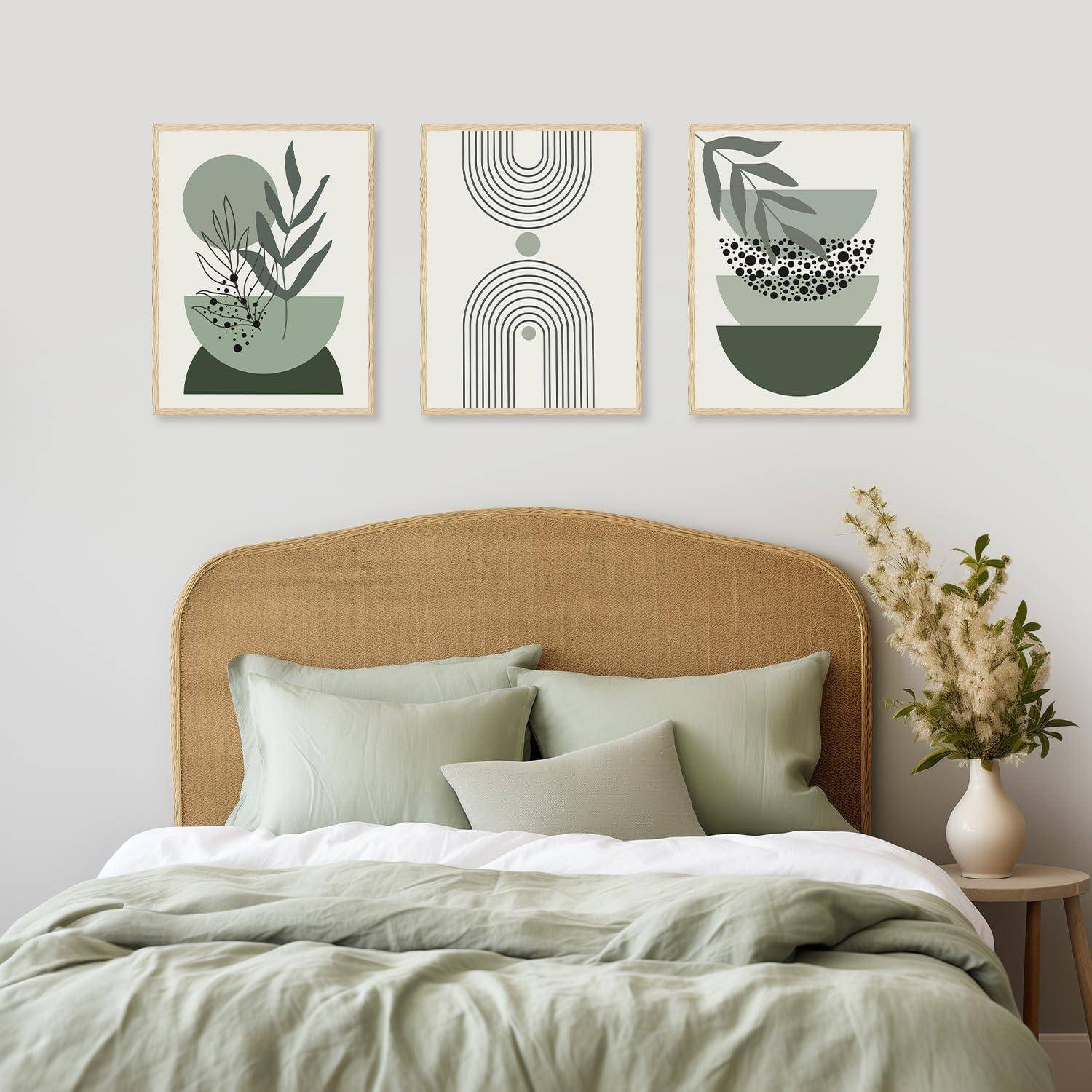 Ein neutral gehaltenes Schlafzimmer zeigt ein Bett mit grünen Kissen und einem hellbraunen Kopfteil. Darüber hängen drei abstrakte Kunstwerke in erdigen Tönen. Neben dem Bett steht ein kleiner Tisch mit einer Vase voller weißer Blumen.