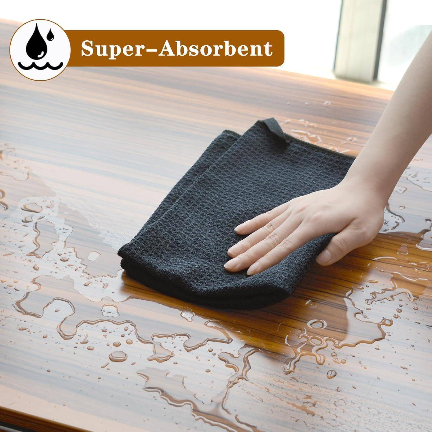 Eine Hand, die mit einem schwarzen Tuch Wasser von einer Holzoberfläche abwischt. Eine Beschriftung zeigt „Super-Absorbent