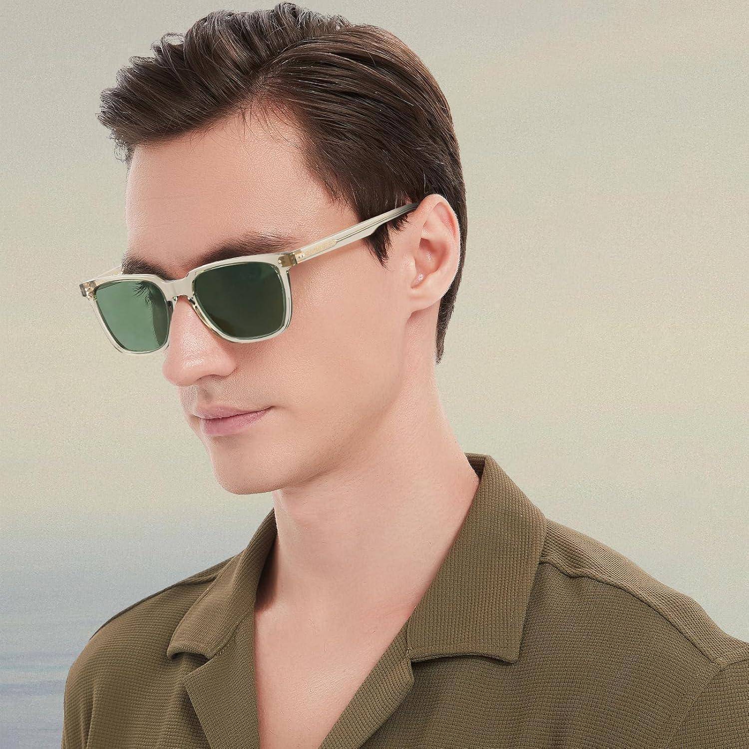 Eine Person mit Sonnenbrille und einem lässigen Hemdkragen blickt zur Seite vor einem neutralen Hintergrund.