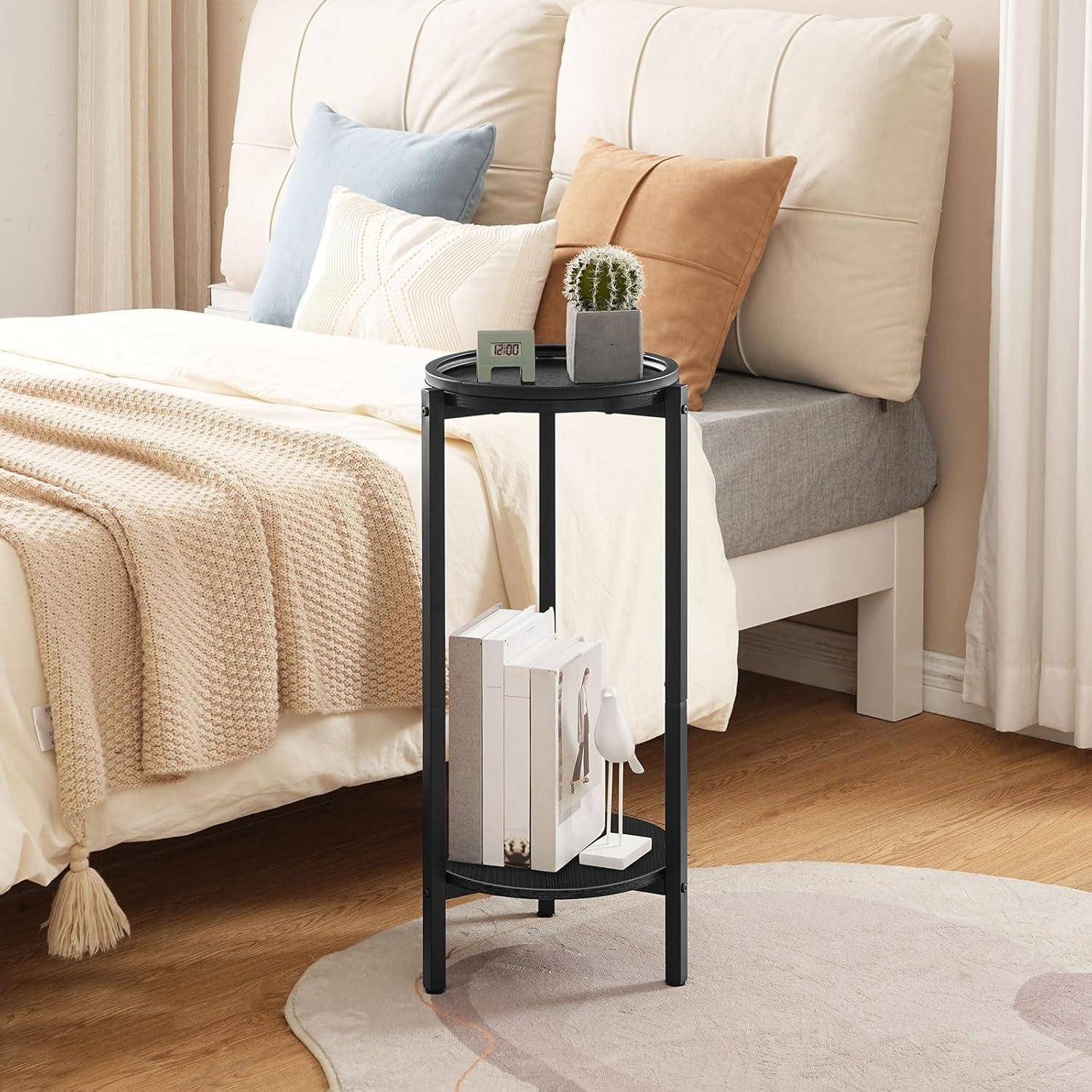 Ein gemütliches Schlafzimmer mit einem beigen Bett, weißen und braunen Kissen und einem kleinen schwarzen Nachttisch, auf dem eine Pflanze und Bücher stehen, auf einem Holzboden.