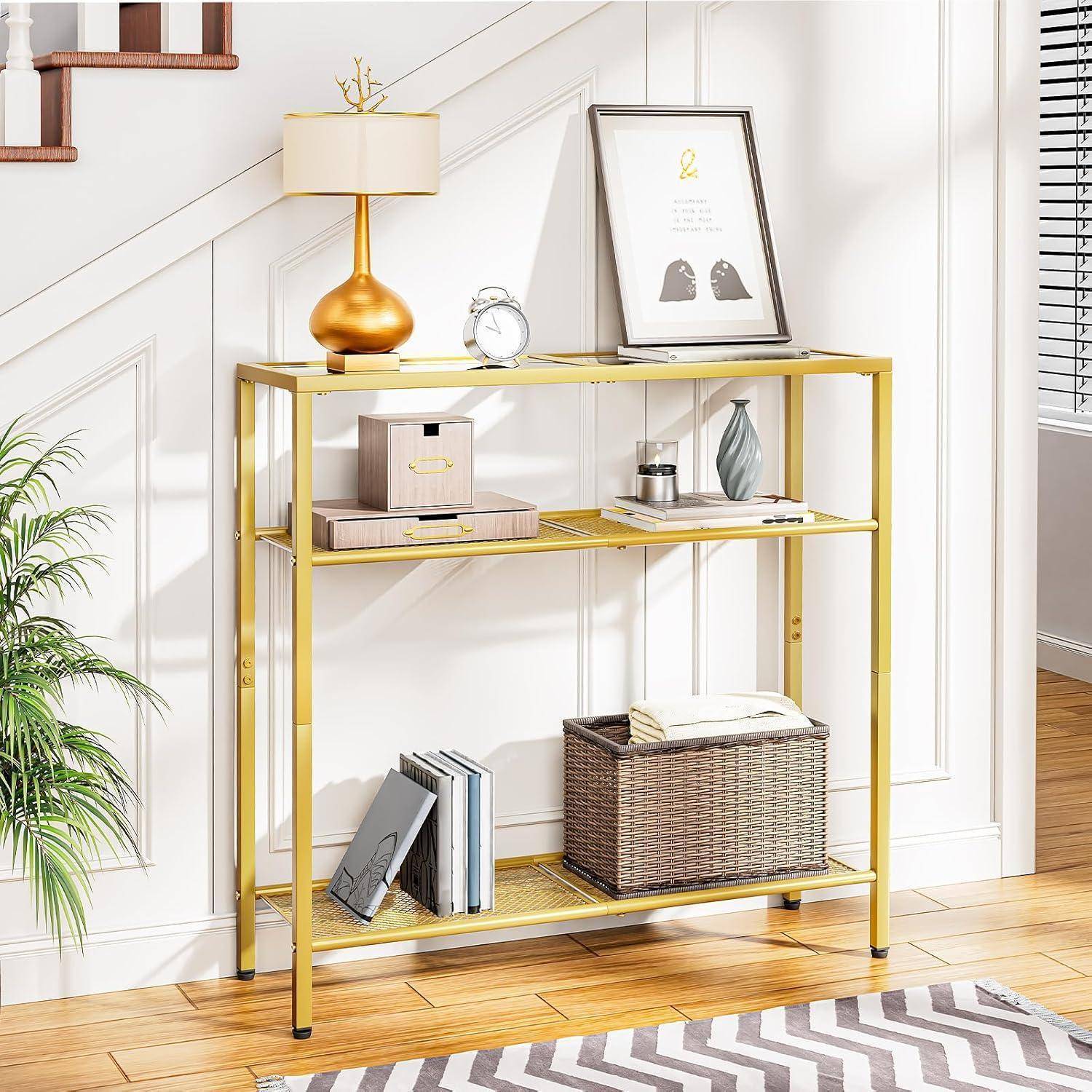 Ein Konsolentisch aus Gold mit einer Lampe und gerahmter Kunst oben, flankiert von Aufbewahrungsboxen und einem Korb, vor einer weißen Wand neben einer Treppe.