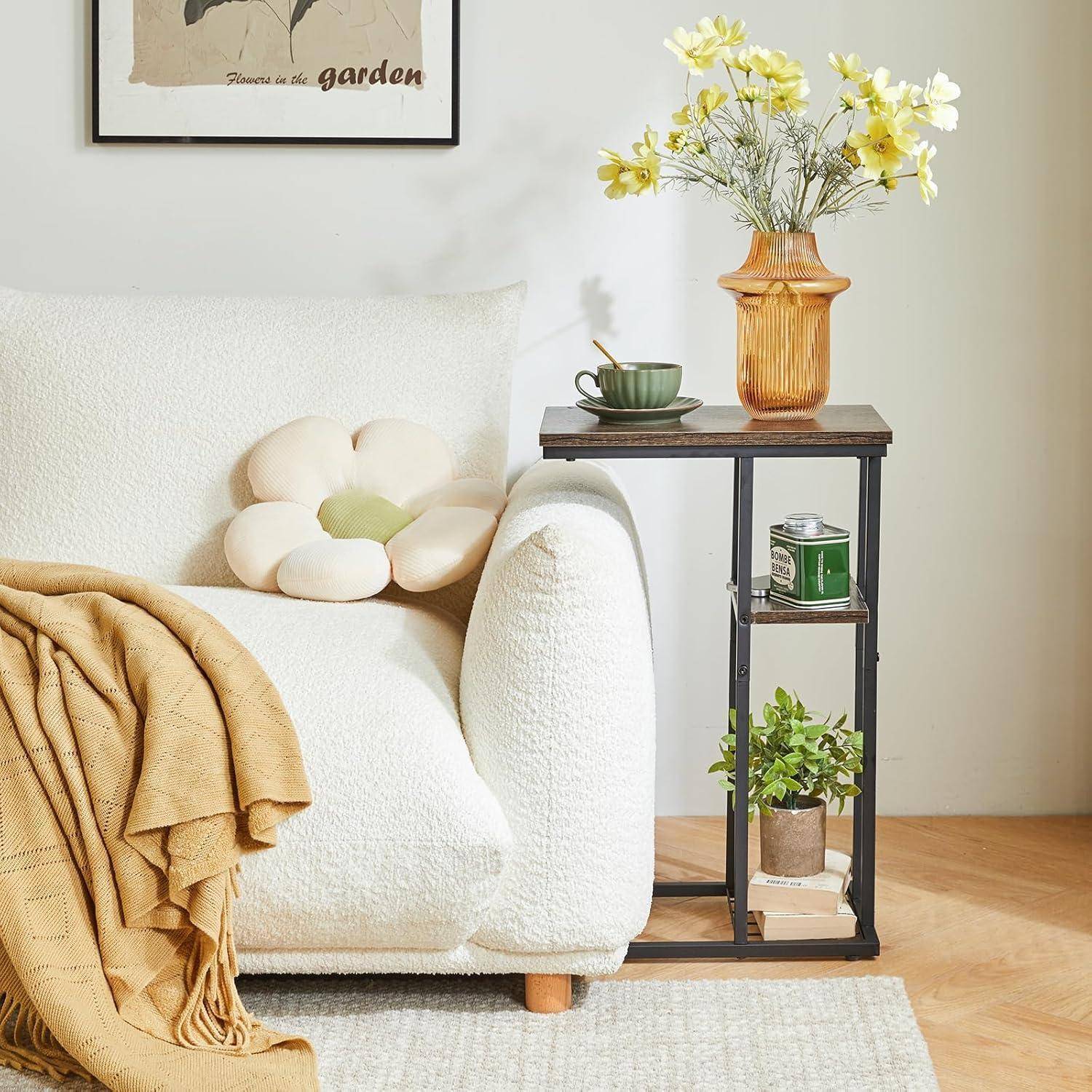 Eine gemütliche Ecke des Wohnzimmers zeigt einen weißen Sessel mit einem weichen Kissen und einer Decke, einen Beistelltisch mit einer Vase voller gelber Blumen, einer Tasse und einer Pflanze.