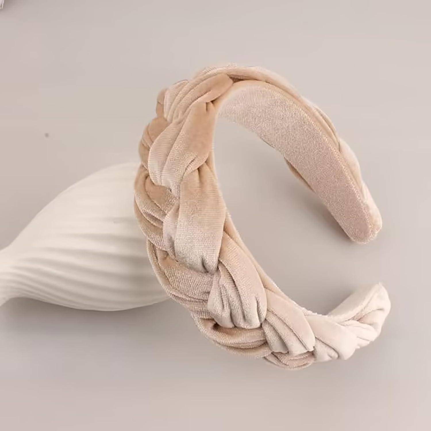Ein beige geflochtenes Haarband aus samtigem Stoff wird präsentiert, ruhend auf einem glatten, muschelartigen Objekt auf einer hellen Oberfläche.