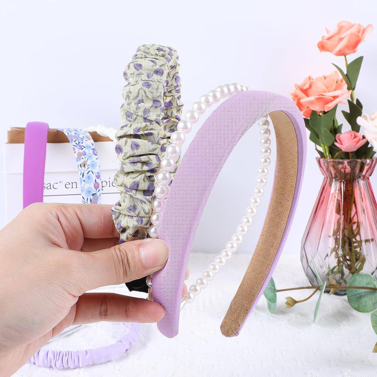 Eine Hand hält ein lila Haarband mit Perlen neben zwei floralen Stoffhaarband. Rosa und orange Blumen in Vasen befinden sich im Hintergrund.