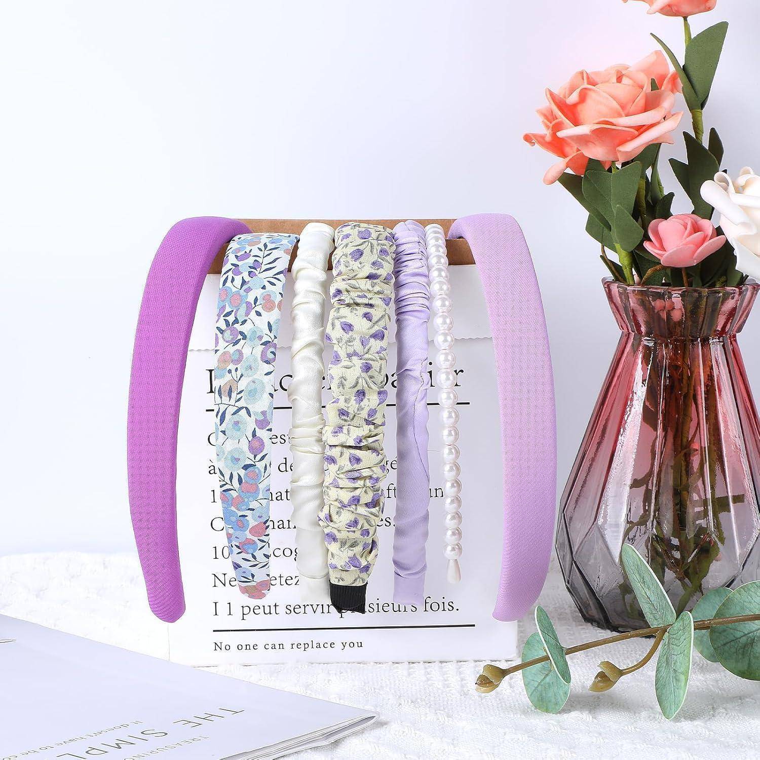 Ein Set dekorativer Haarreifen, die auf einem Holzständer neben einer Vase mit rosa und weißen Blumen auf einer weißen Tischdecke ausgestellt sind.