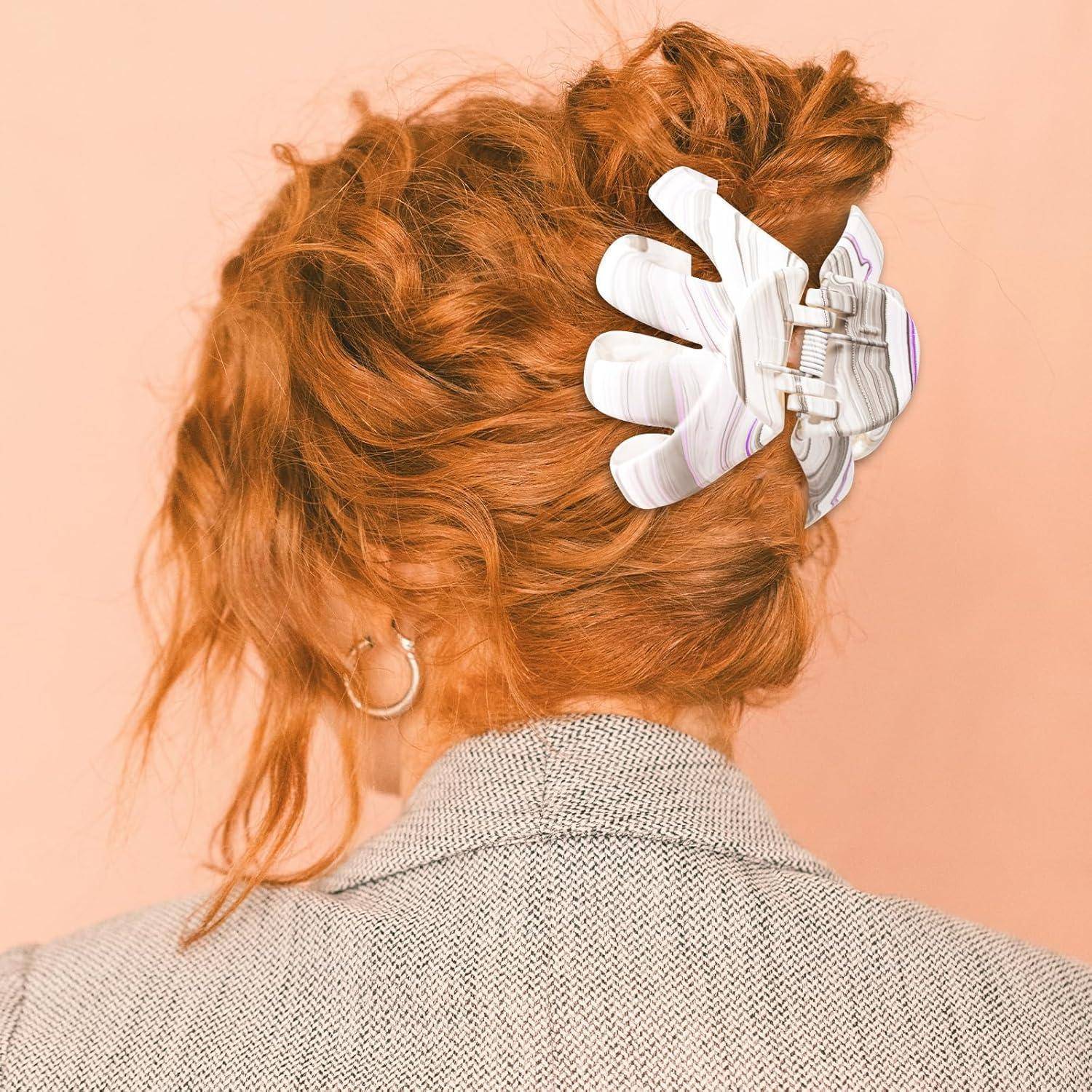 Eine Person mit lockigem roten Haar wird von hinten gezeigt, die eine große weiße Haarspange in Form von Fingern vor einem pfirsichfarbenen Hintergrund trägt.